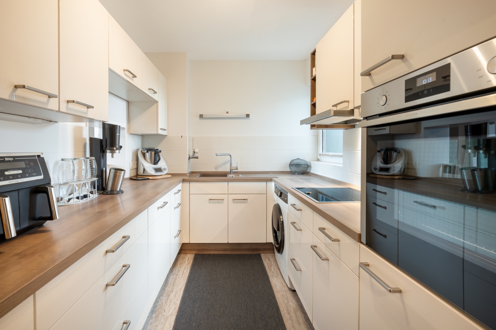 Moderne Einbauküche mit weißen Schränken, Holzarbeitplatte und Elektrogeräten.