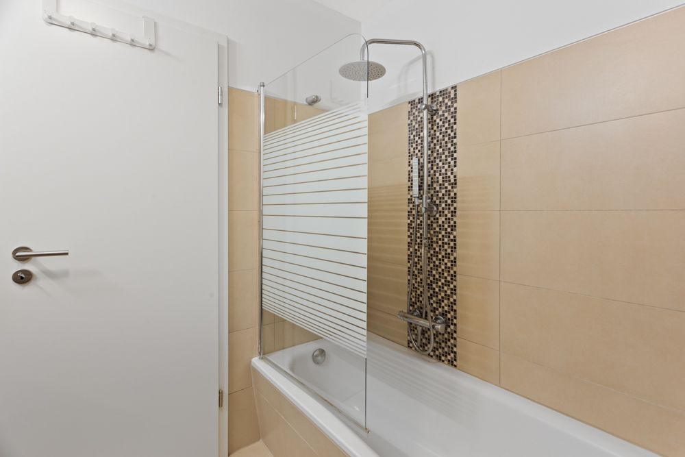 Modernes Badezimmer mit Badewanne, Glasduschwand und beigefarbenen Fliesen.