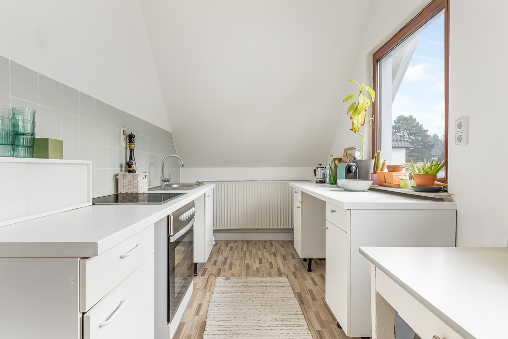 Helle Küche mit weißen Schränken, großem Fenster und Pflanzen auf der Fensterbank.
