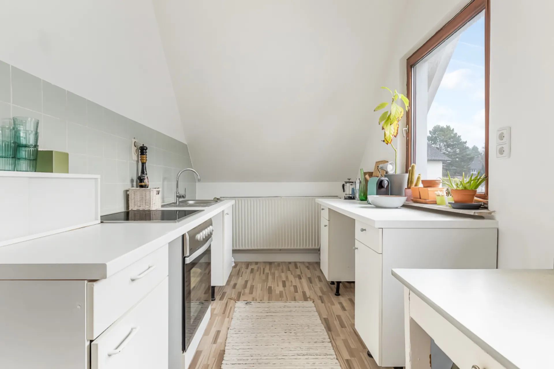 Helle Küche mit weißen Schränken, großem Fenster und Pflanzen auf der Fensterbank.