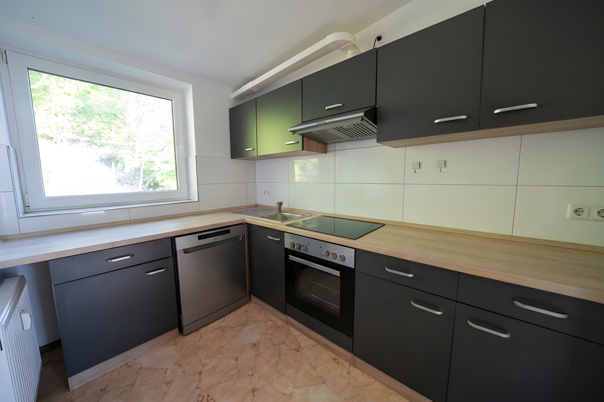 Moderne Küche mit grauen Schränken, großem Fenster, Herd und Spülmaschine.
