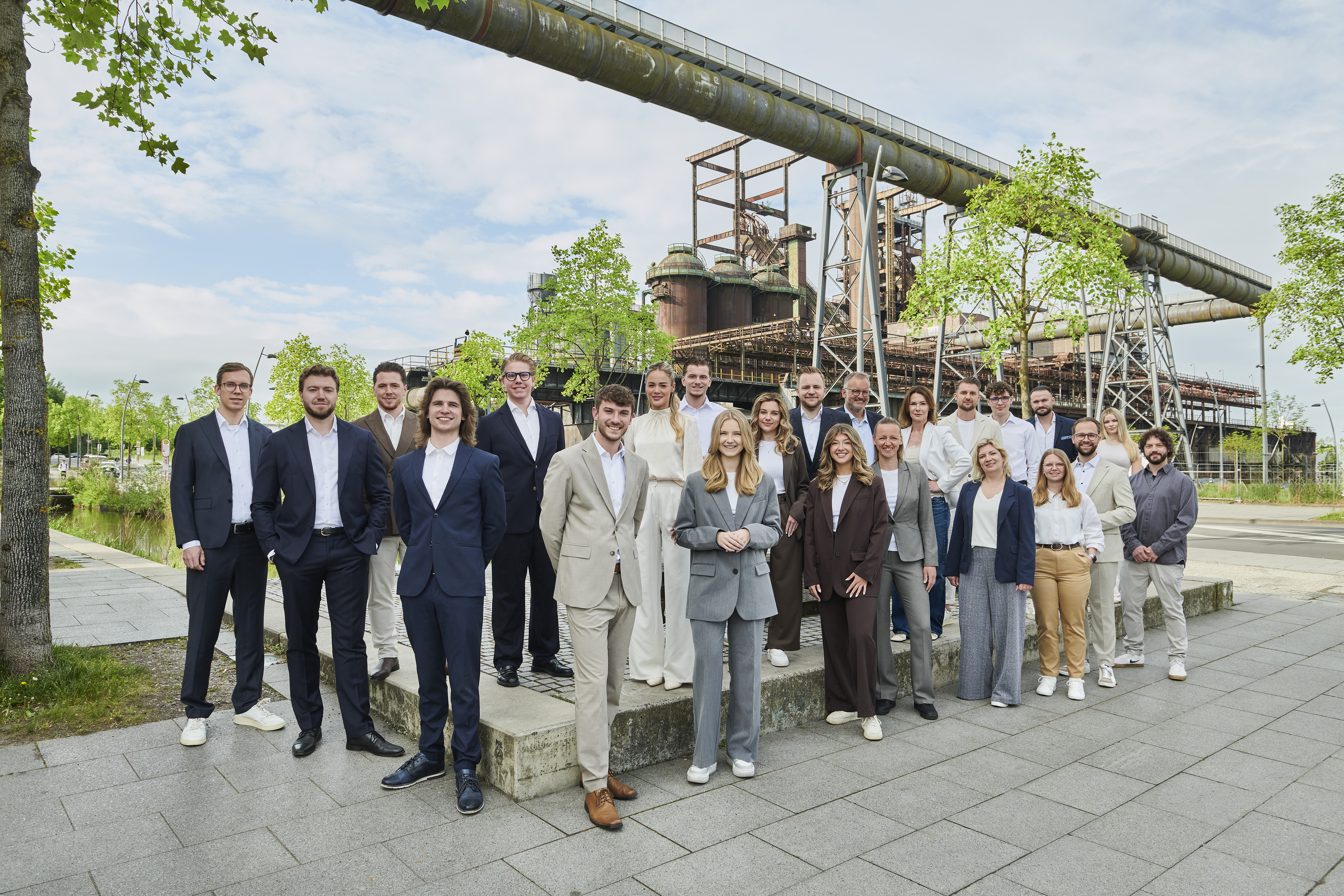 Eine Gruppe von Menschen steht draußen vor einer Industrieanlage und lächelt in die Kamera.