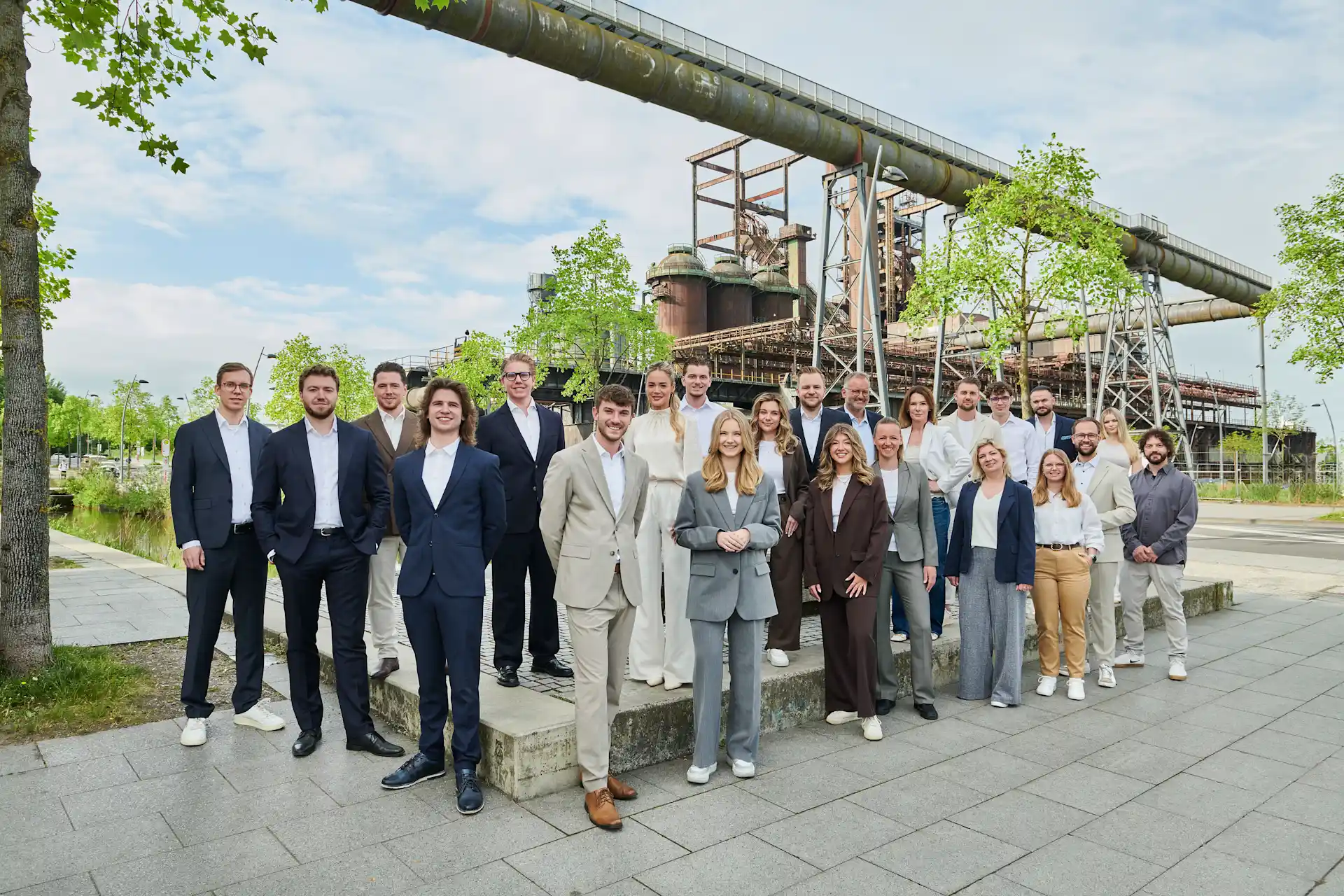 Eine Gruppe von Menschen steht draußen vor einer Industrieanlage und lächelt in die Kamera.