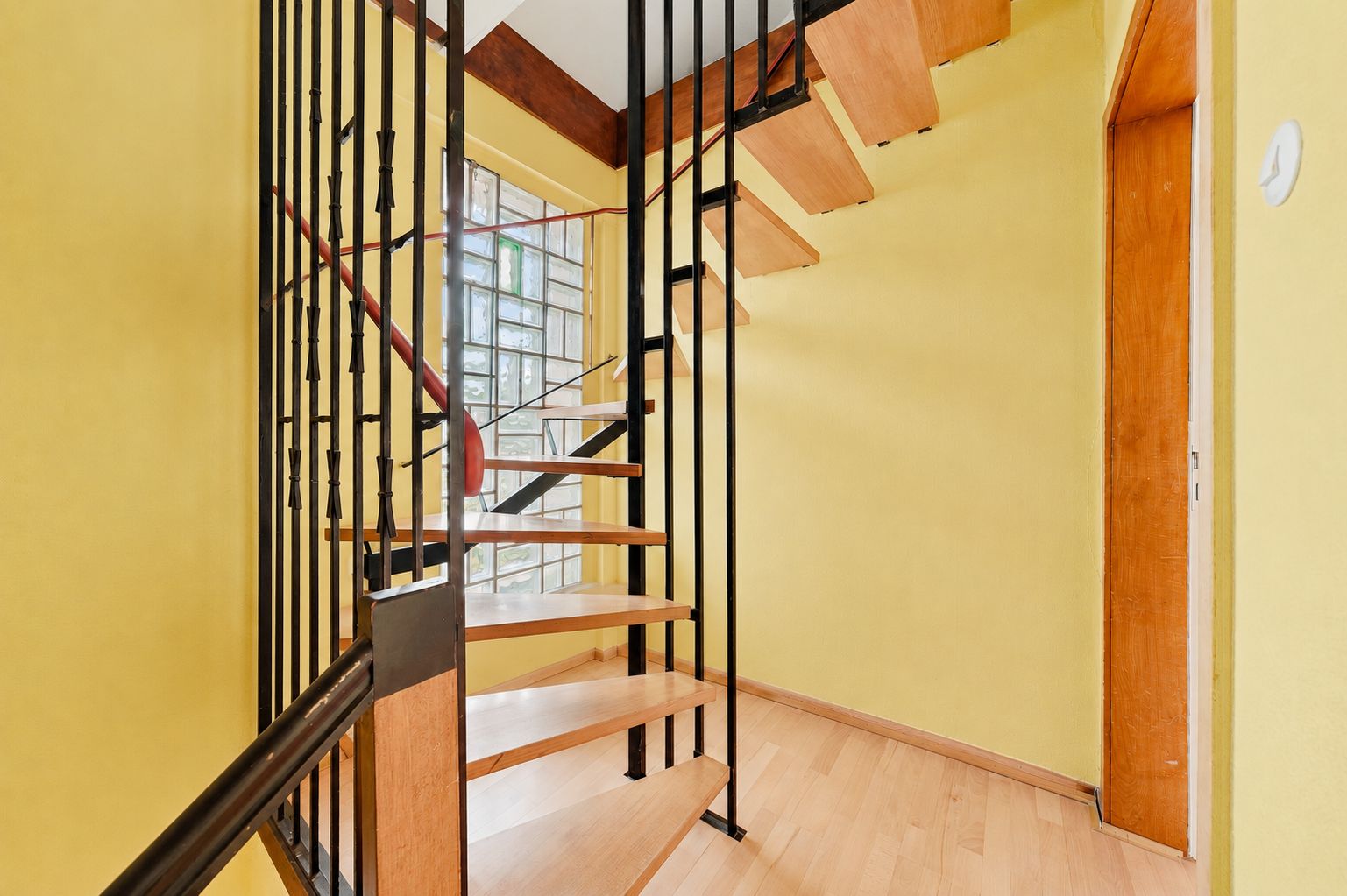 Holztreppe mit schwarzem Geländer in einem Flur mit gelben Wänden und Holztür.