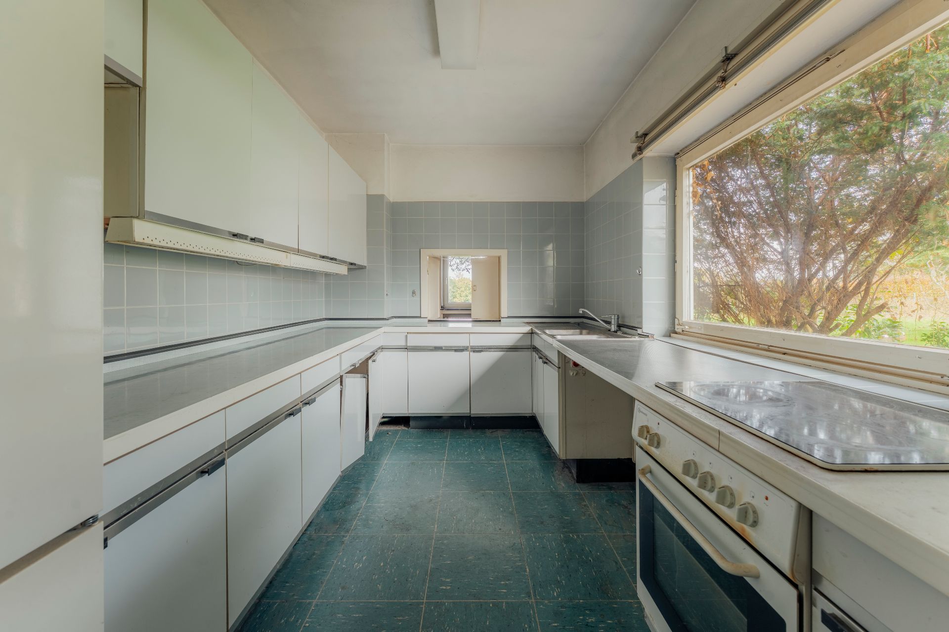 Helle Küche mit weißen Schränken, großem Fenster und grünem Boden.
