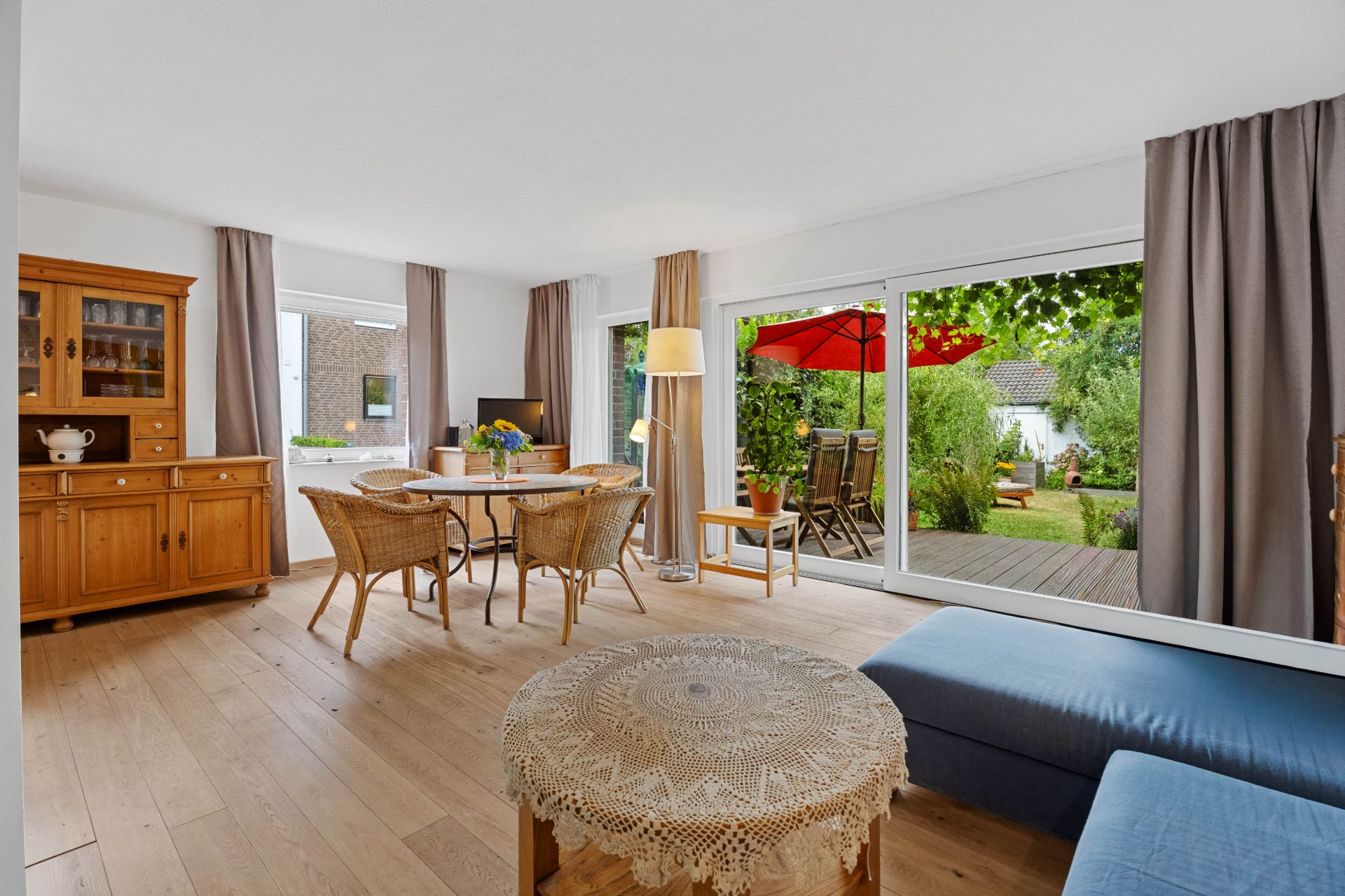Heller Wohnbereich mit Holzmöbeln, Esstisch, Sofa und Blick auf eine Terrasse mit Garten.