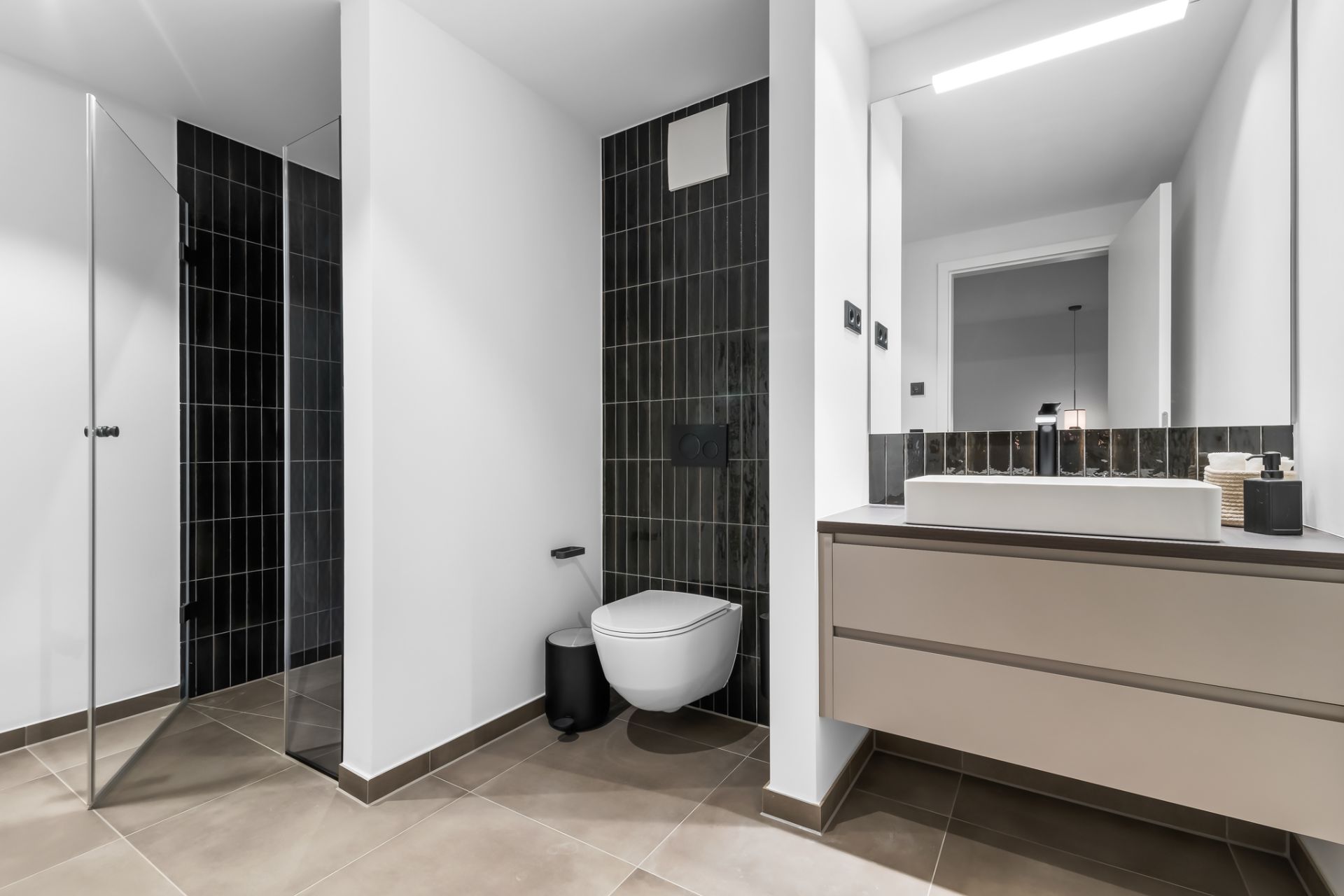 Modernes Badezimmer mit Wandtoilette, Duschkabine und großem Spiegel über dem Waschbecken.