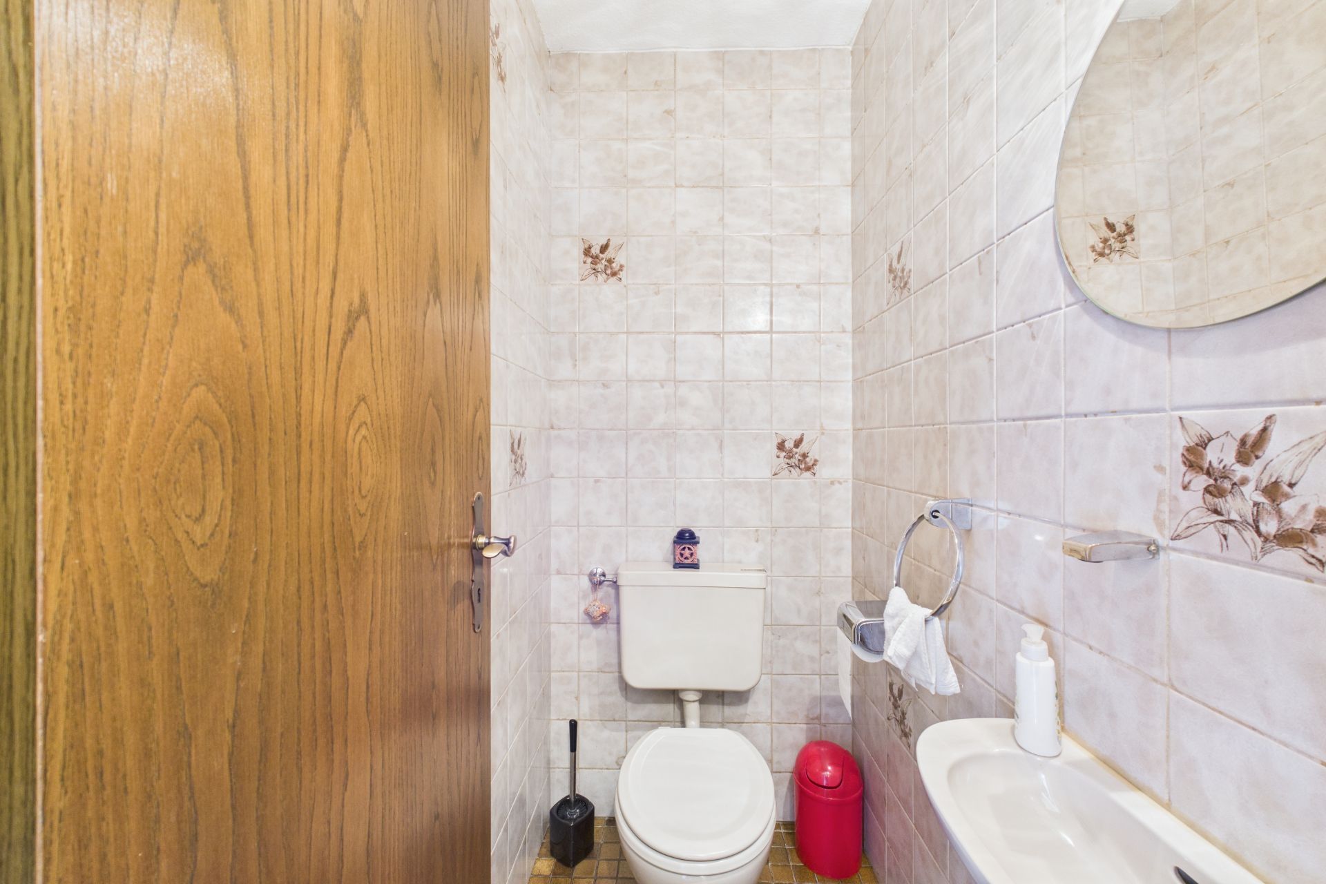 Kleine Toilette mit WC, Waschbecken, Spiegel und Fliesen mit Blumenmuster.
