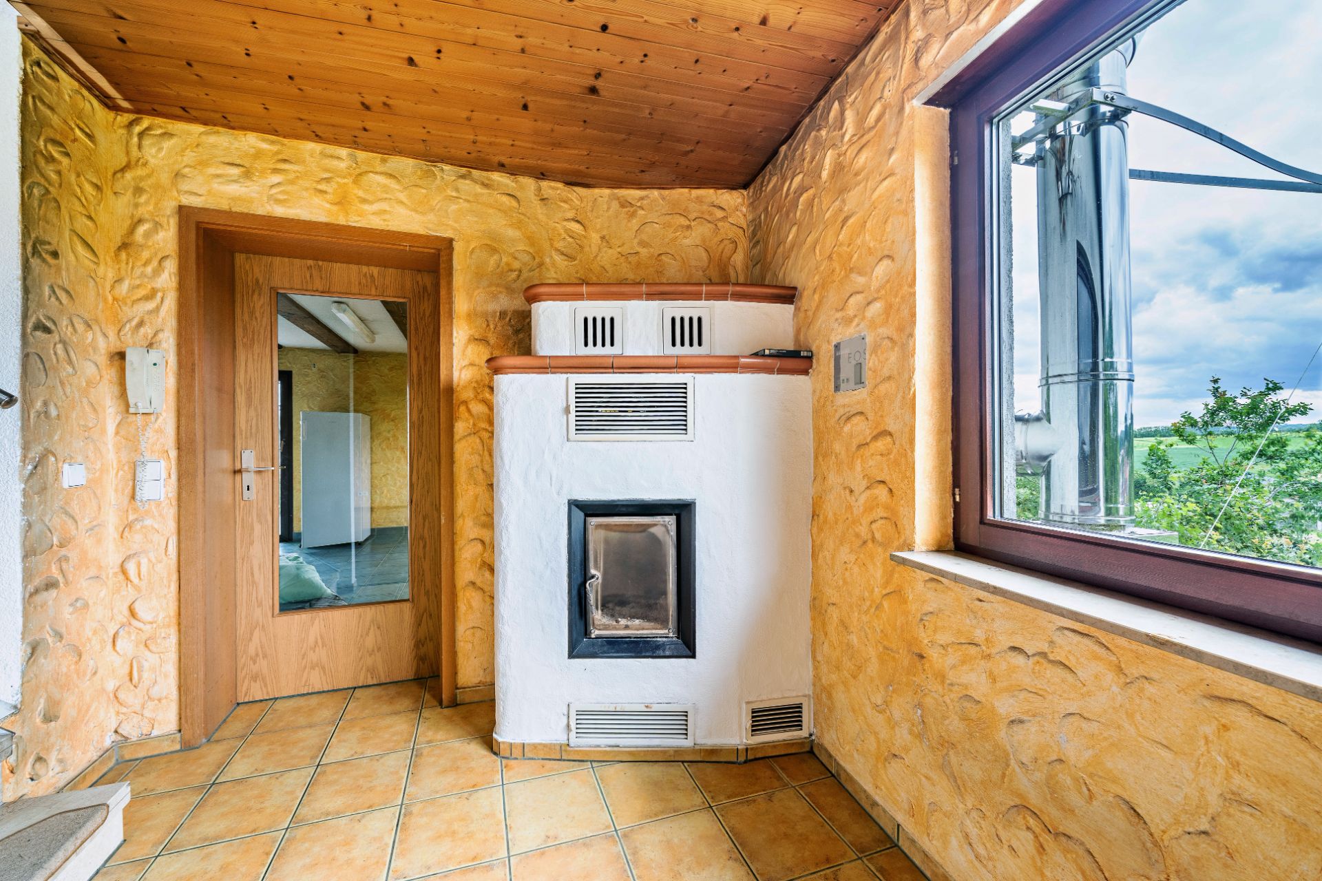 Raum mit gemauertem Kamin, gelben Wänden, Fenster und Holztür mit Spiegel.