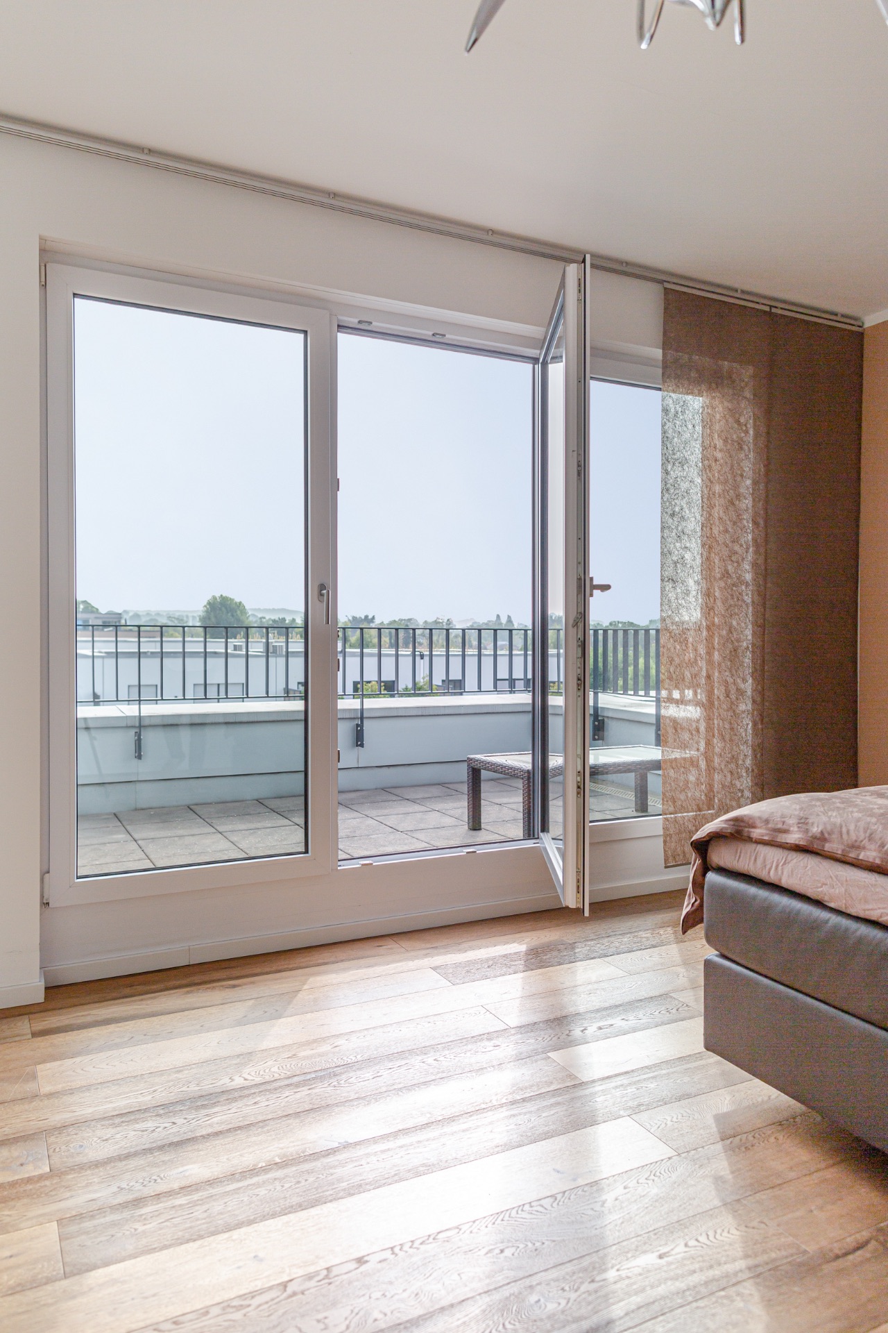 Offene Glastür führt von einem Zimmer auf eine Terrasse mit Geländer.