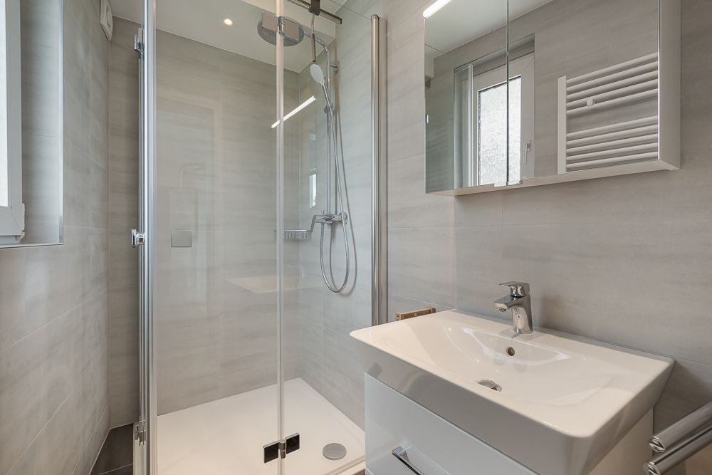 Modernes Badezimmer mit Glasdusche, Waschbecken und Spiegel, alles in hellen Farben.