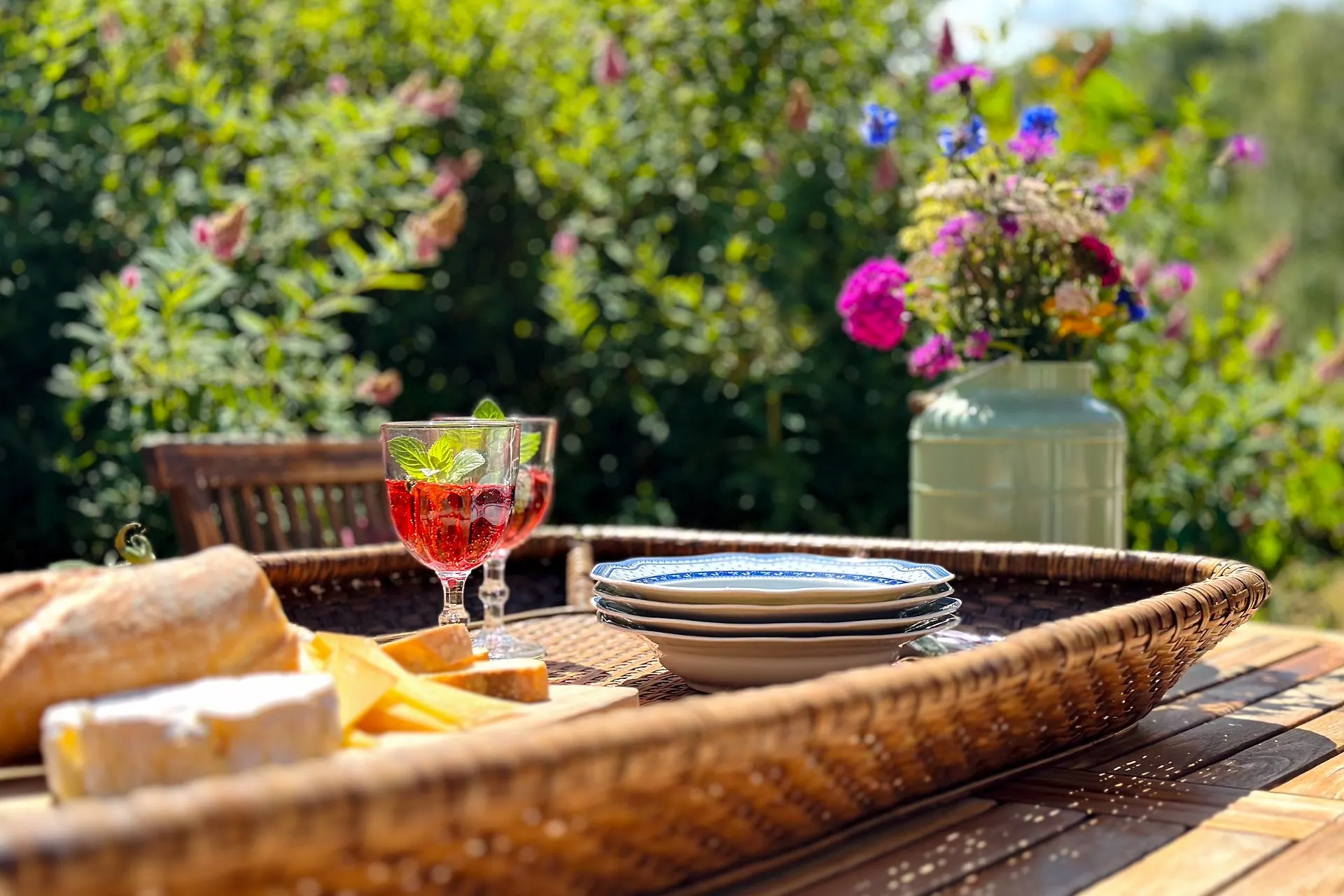 Tisch im Garten mit Gläsern, Tellern, Käse, Brot und einer Vase mit Blumen.