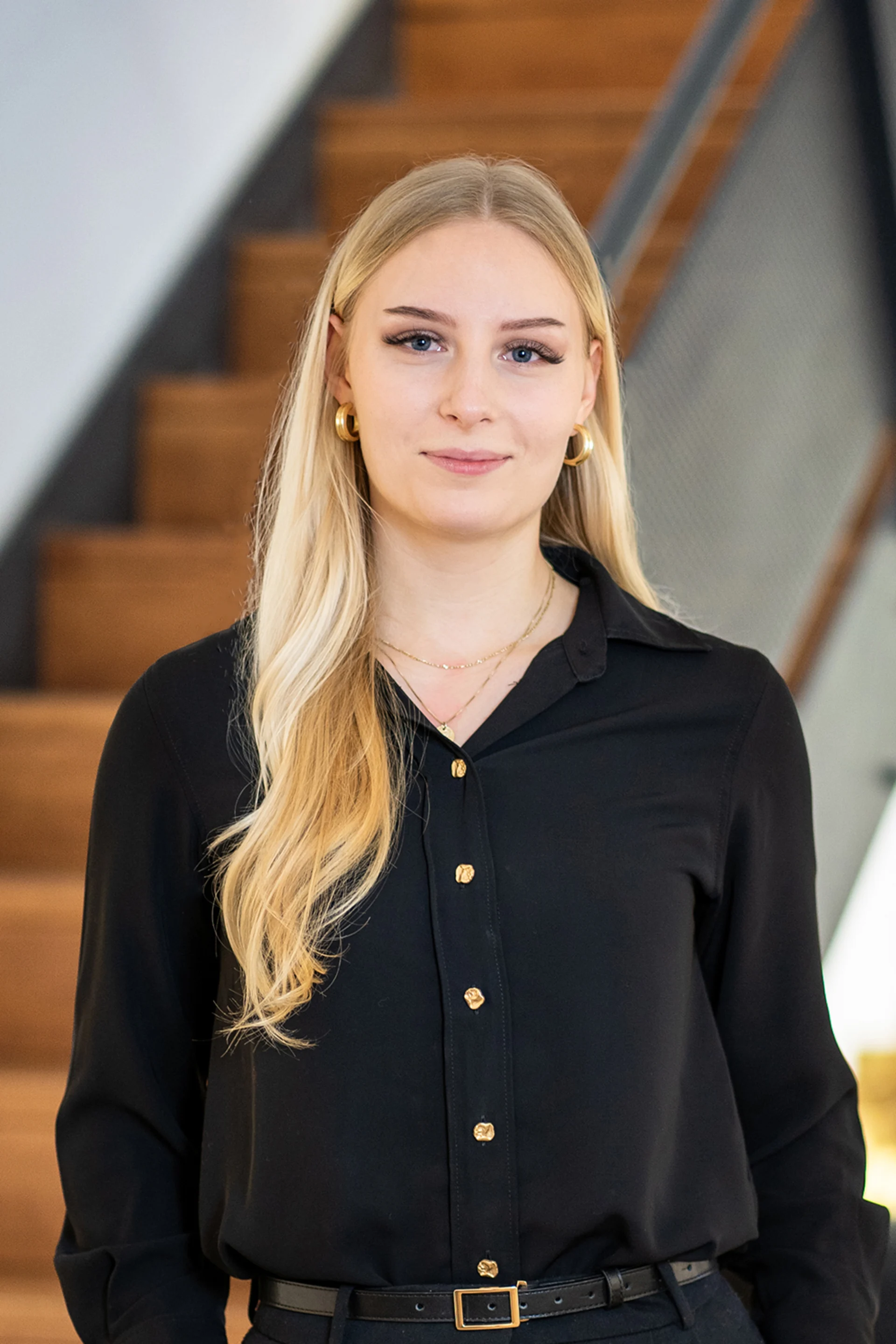 Eine junge Frau mit langen blonden Haaren steht vor einer Holztreppe.