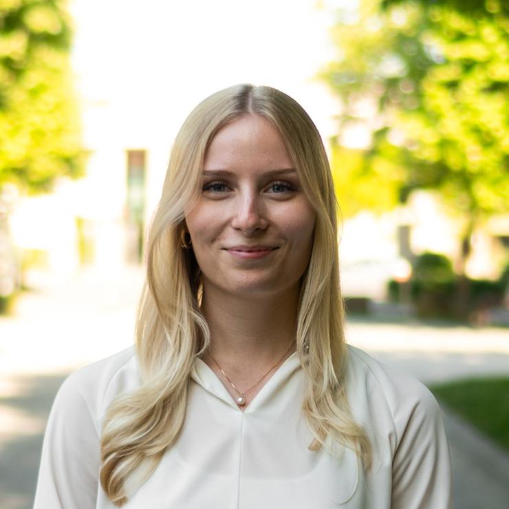 Eine junge Frau mit langen blonden Haaren steht vor einer Holztreppe.