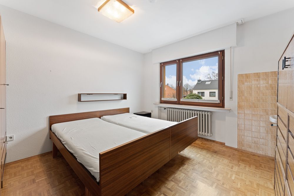 Schlafzimmer mit Doppelbett, großem Fenster, Holzfußboden und Heizung unter dem Fenster.
