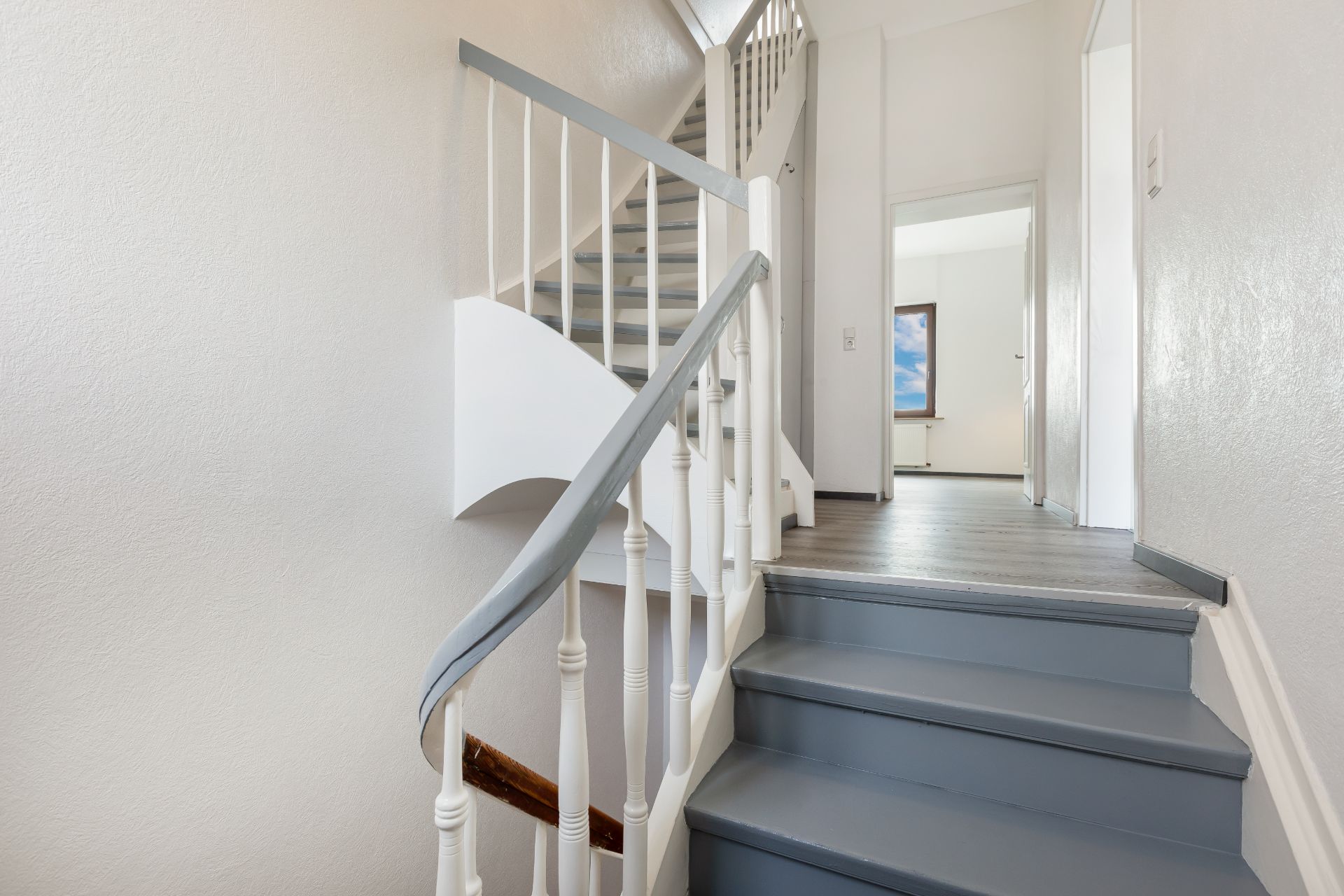 Treppenhaus mit weißen Wänden, grauen Stufen und Geländer in einem Wohnhaus.