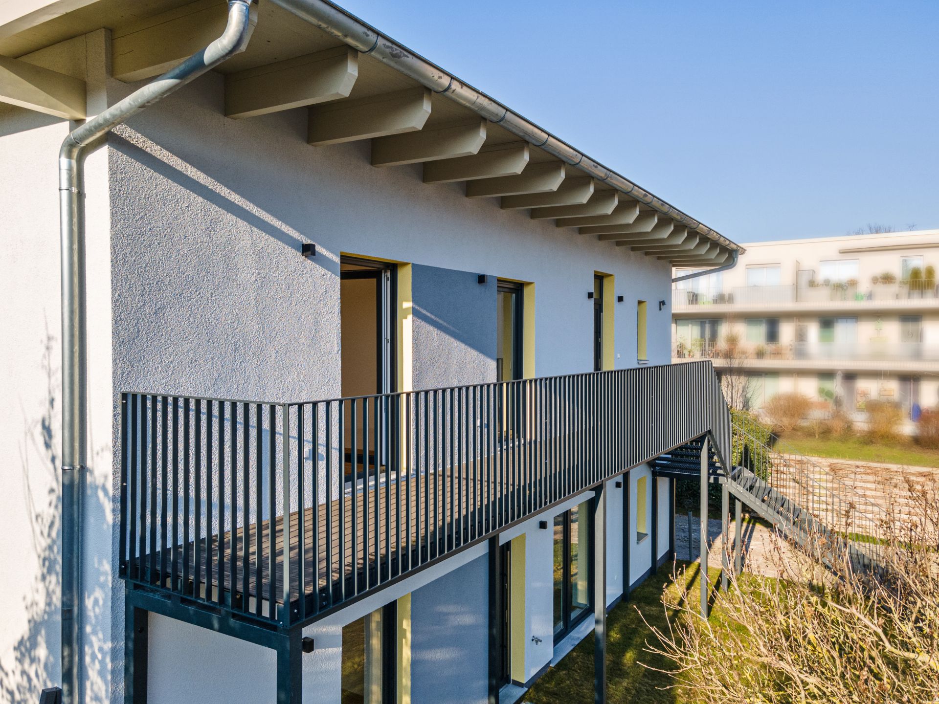 Modernes Wohngebäude mit Außentreppe und Metallgeländer im Obergeschoss.