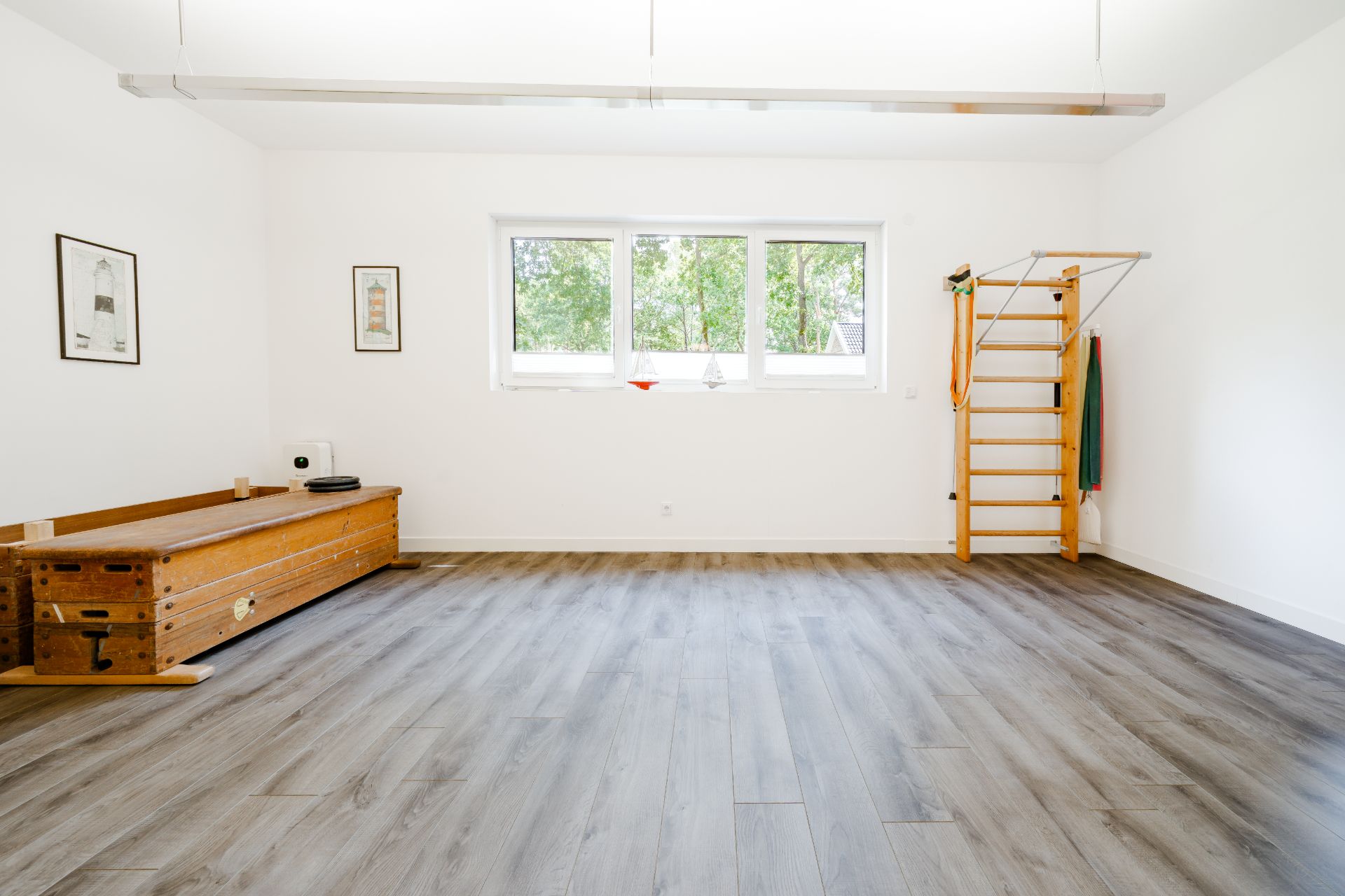 Heller Raum mit Holzboden, Sprossenwand und Turnbank, großes Fenster an der Rückwand.