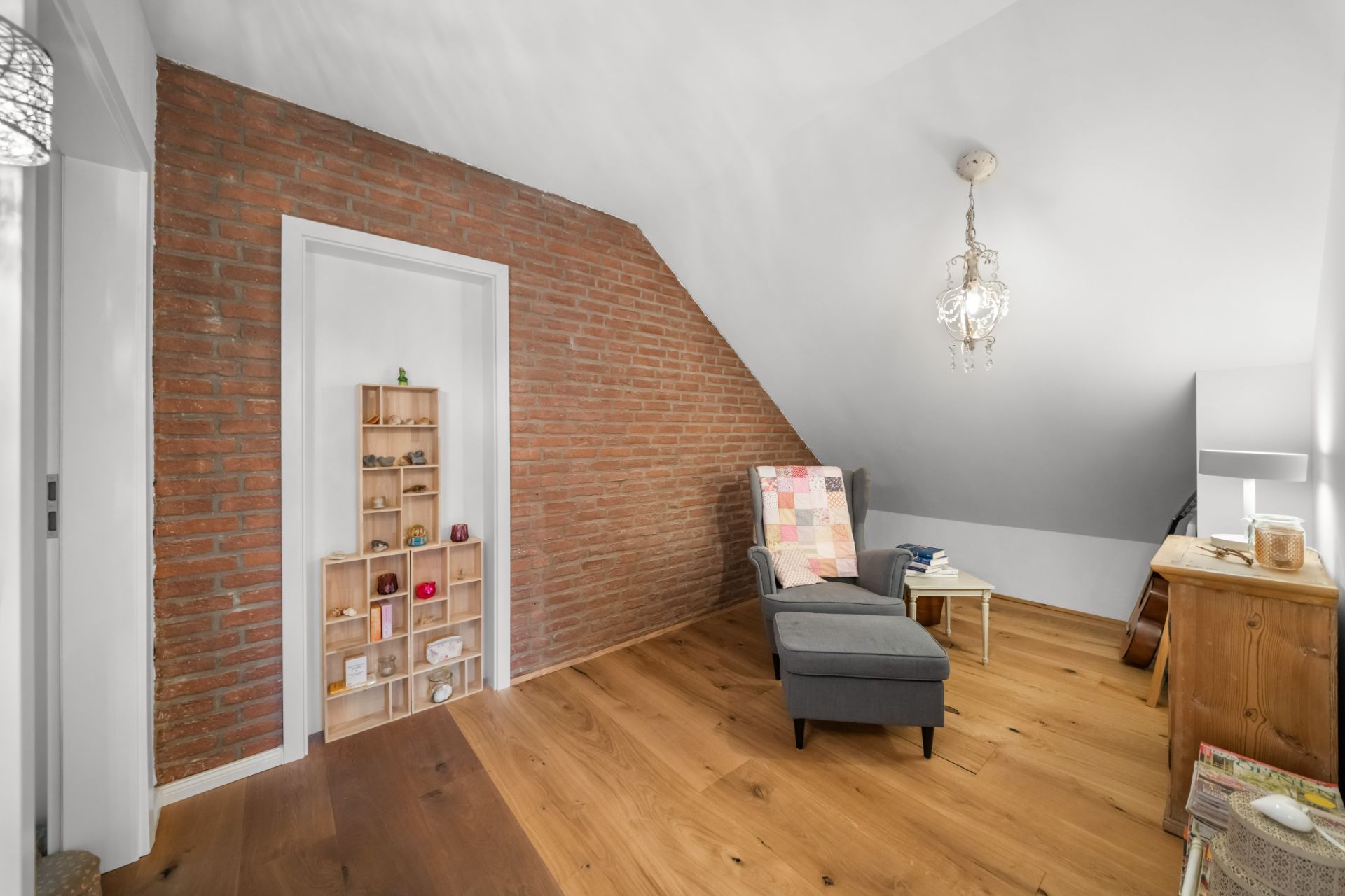 Wohnraum mit Backsteinwand, Sessel, Holzregal und Holzfußboden.