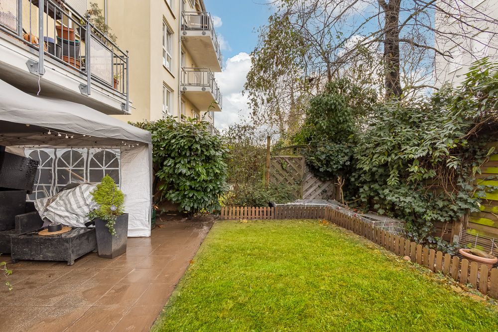 Grüne Wiese mit kleinem Holzzaun und Terrasse neben einem Wohnhaus.