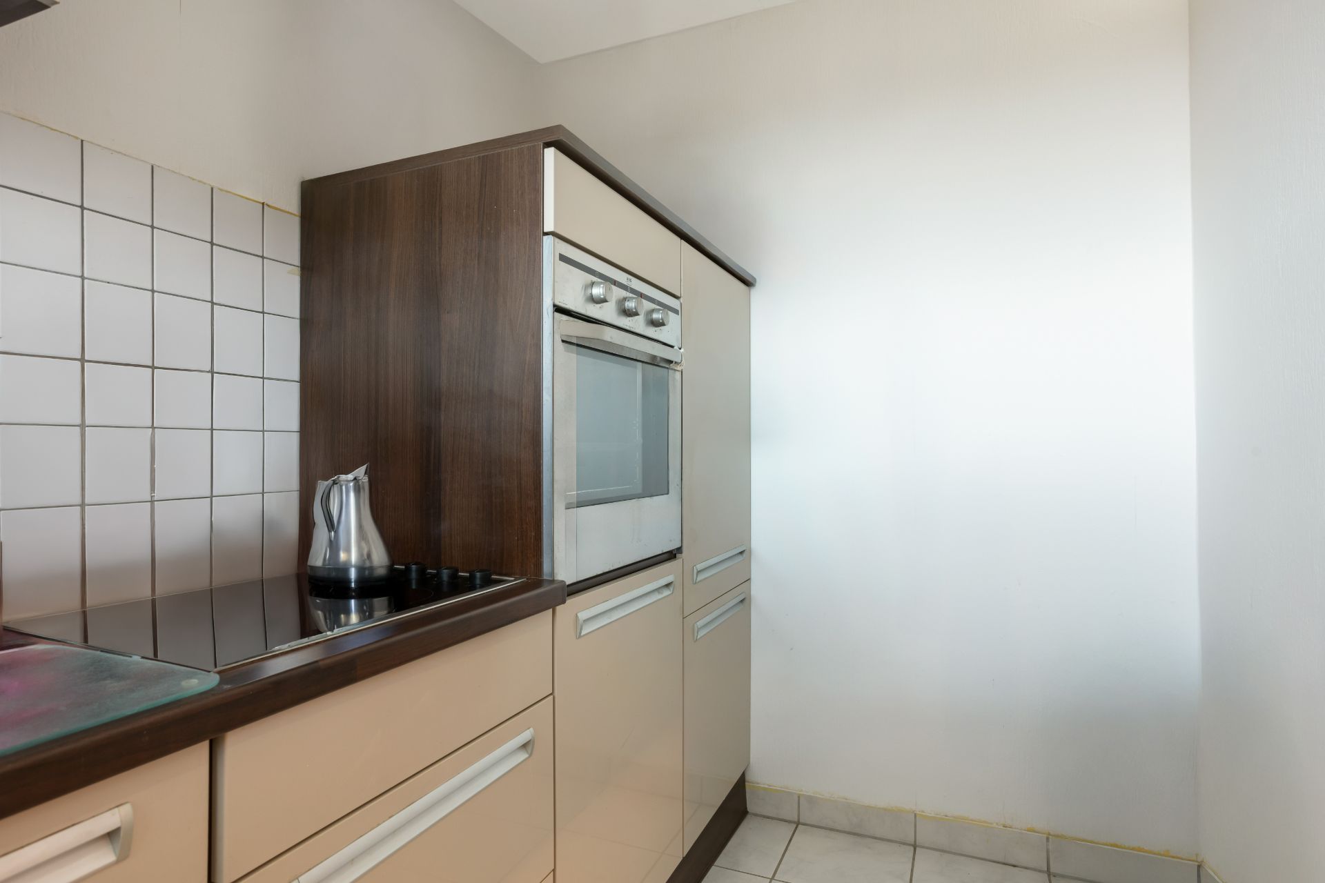 Moderne Küche mit Einbauherd, Cerankochfeld und Wasserkocher, helle Fliesen an der Wand.