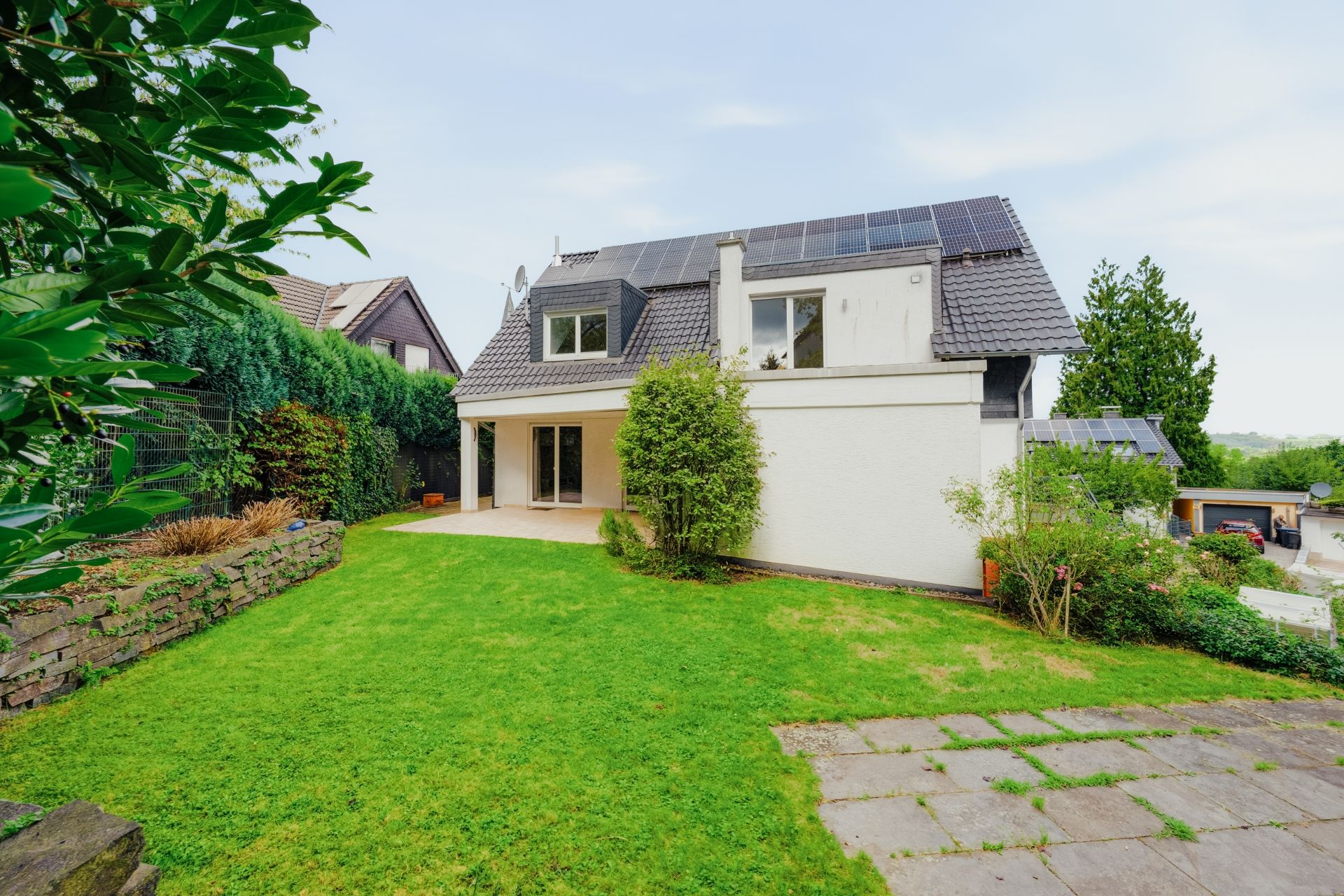 Modernes Einfamilienhaus mit Solarpanelen und Garten, Sicht auf Terrasse und Grünfläche.