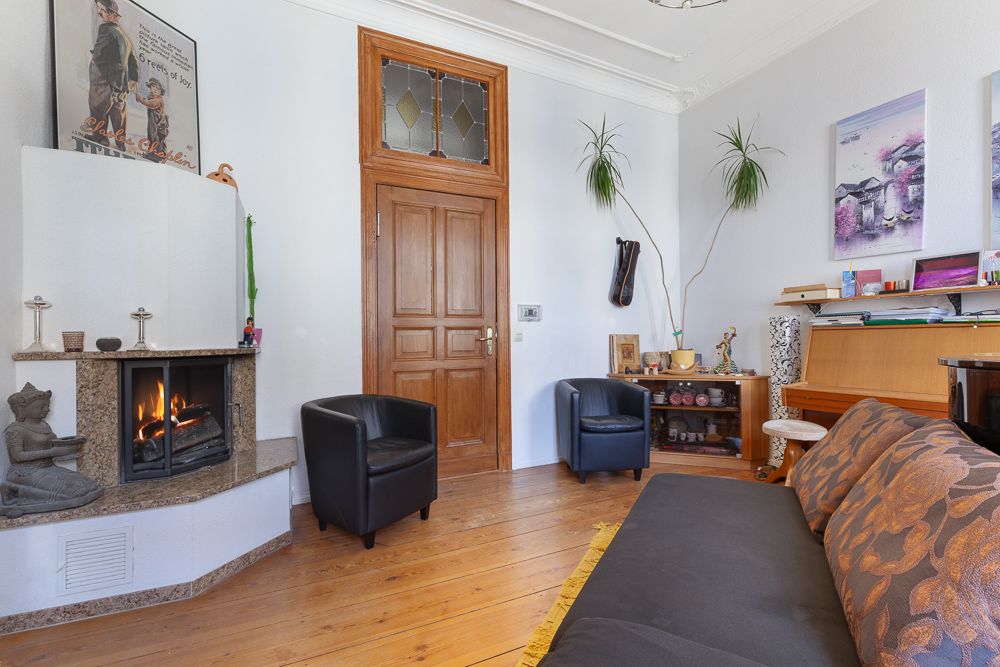 Wohnzimmer mit Kamin, Holztür, zwei Sesseln, Sofa, Klavier und Pflanzen.