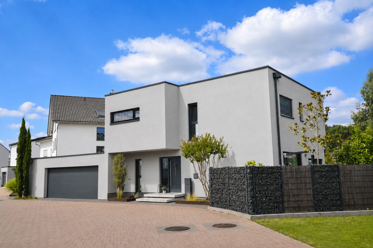 Modernes Einfamilienhaus mit Flachdach, großer Garage und Vorgarten an einer gepflasterten Straße.