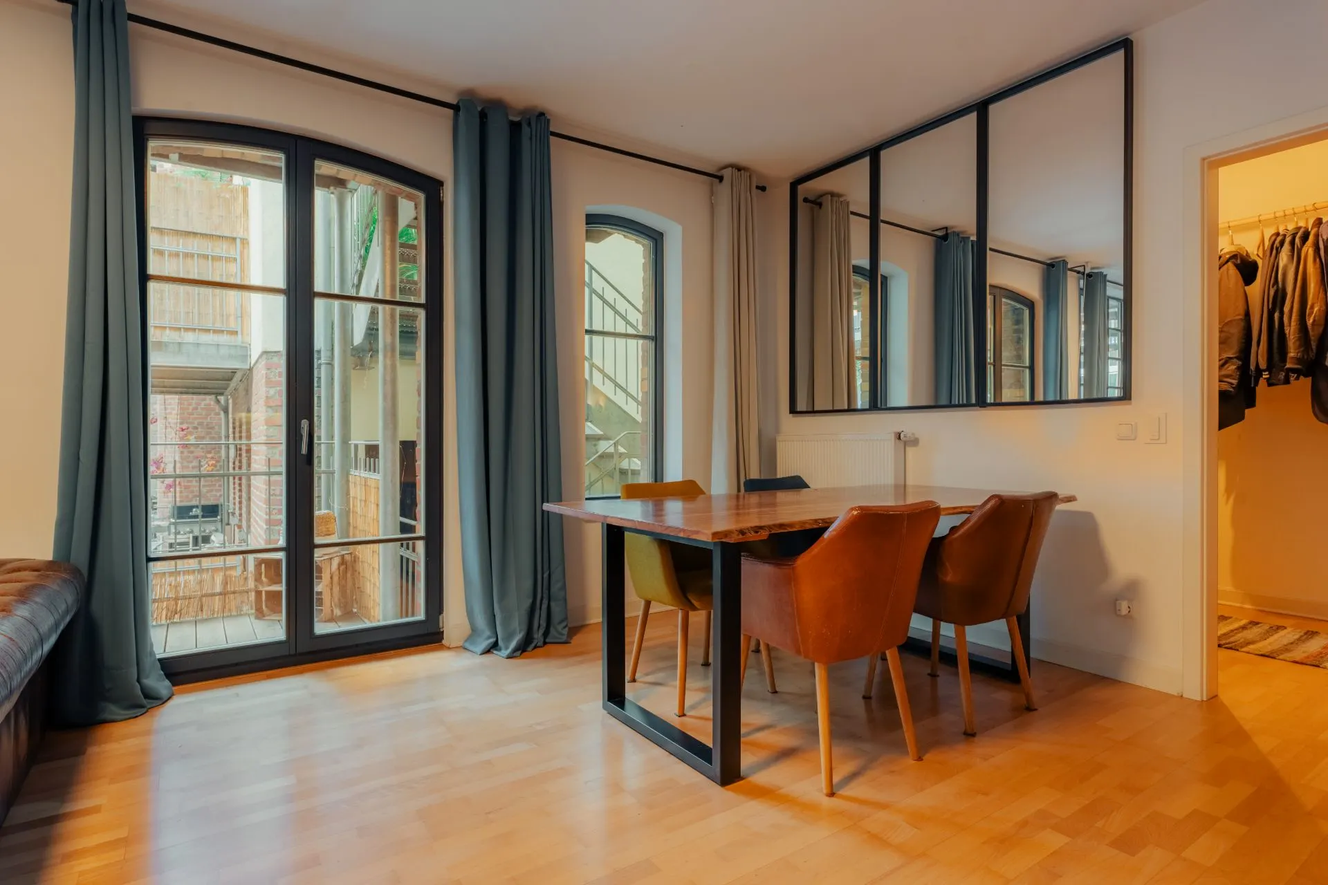 Essbereich mit Holztisch und vier Stühlen neben großen Fenstern und Spiegel an der Wand.