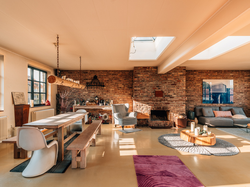 Helles Wohnzimmer mit Ziegelwand, Esstisch, Sofaecke, Kamin und Oberlichtern.