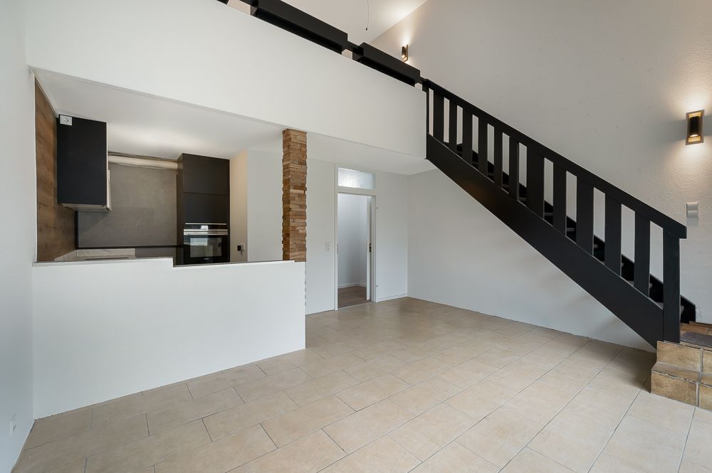 Wohnzimmer mit offener Küche, Treppe und hellen Fliesenboden.