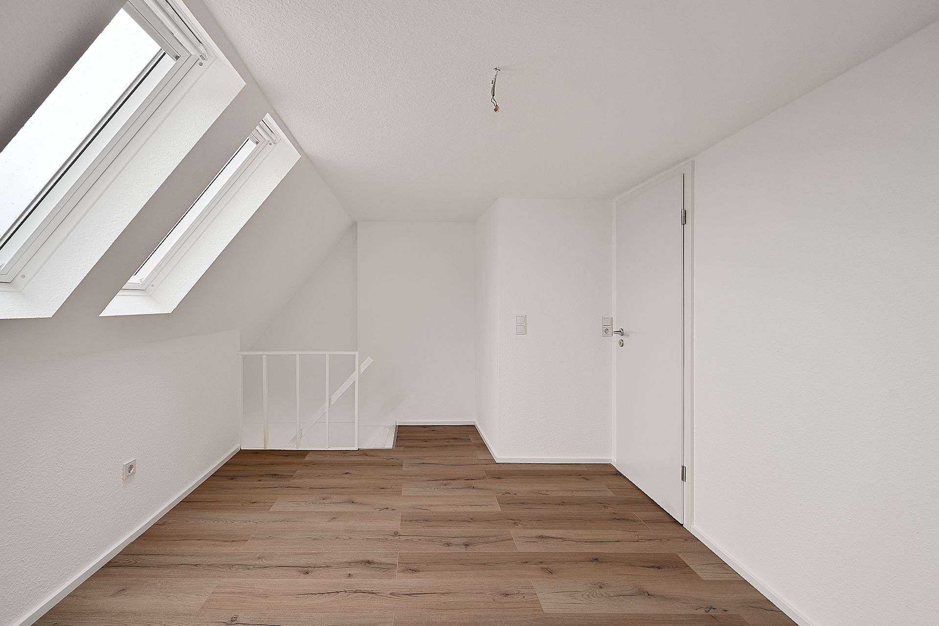 Heller Raum mit Dachfenstern, weiß gestrichenen Wänden und Holzfußboden.