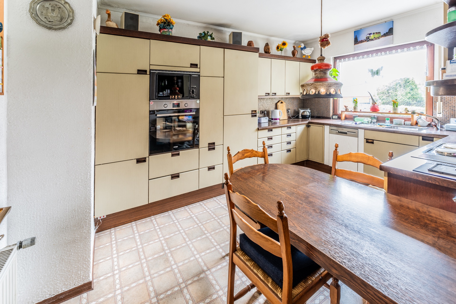 Helle Küche mit Holztisch, Stühlen, Einbauschränken und großem Fenster.