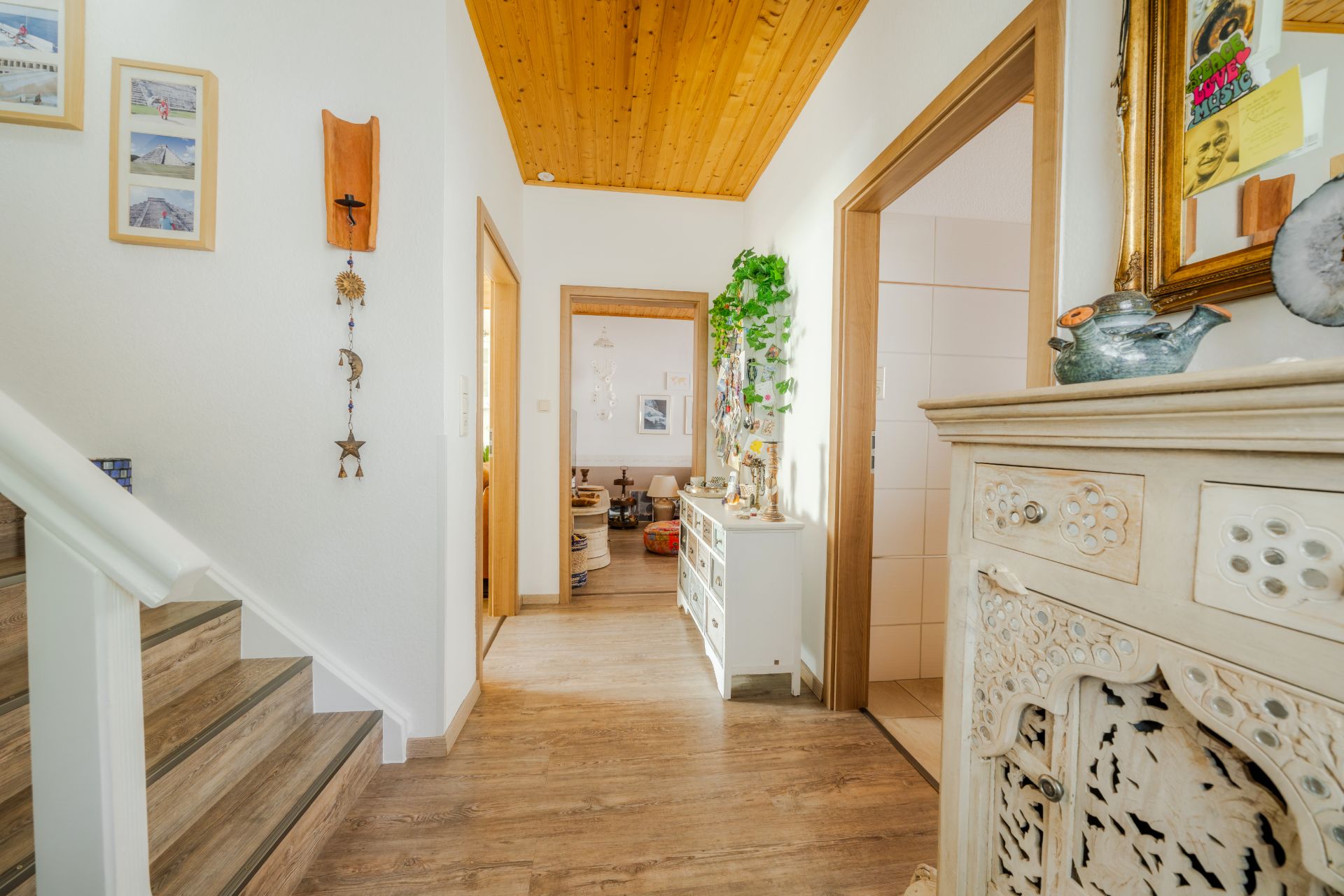 Heller Flur mit Holzboden, Treppe links, zwei offenen Türen und Dekoration an den Wänden.