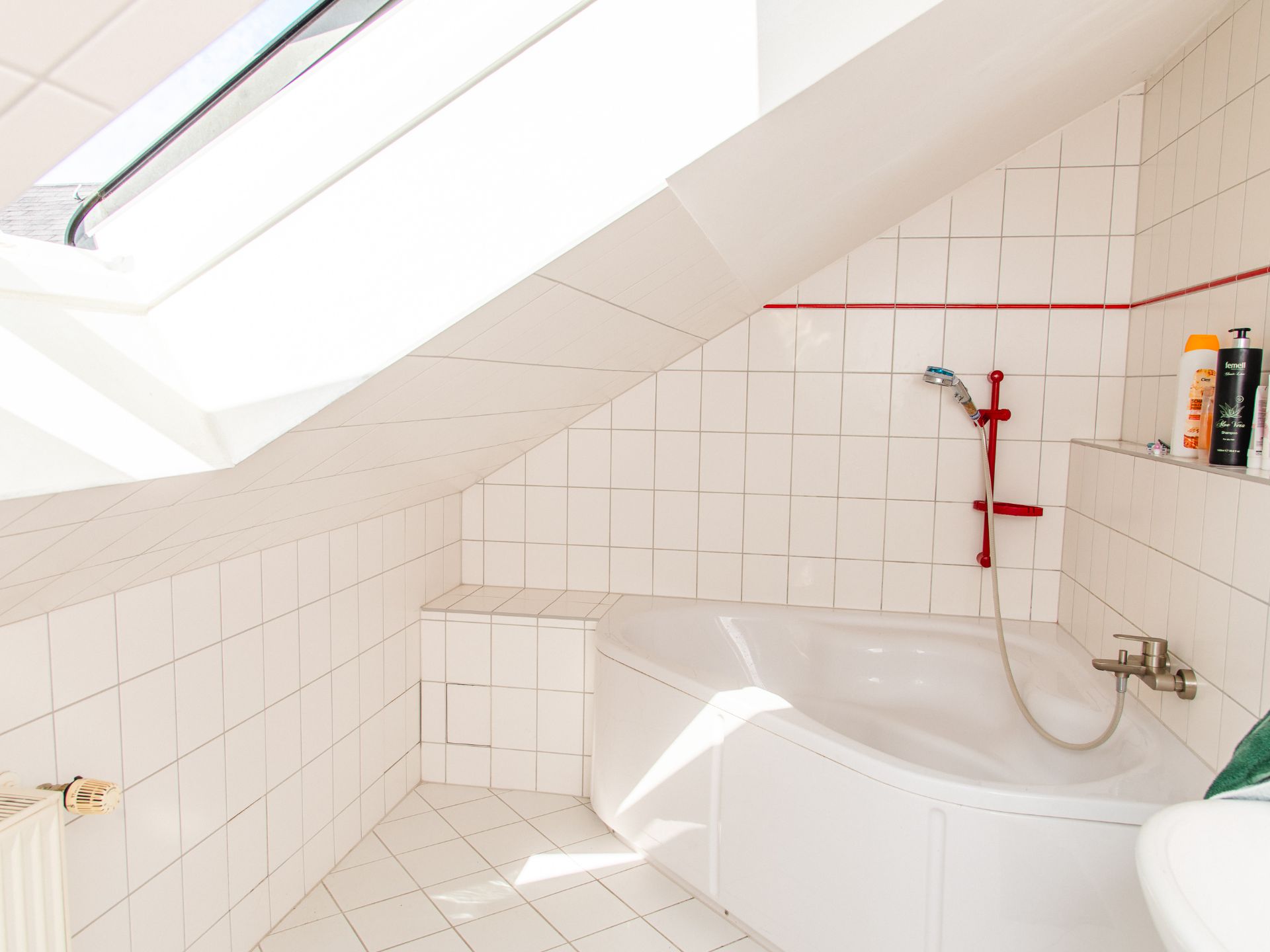 Helles Badezimmer mit Eckbadewanne unter Dachschräge und weiß gefliesten Wänden.
