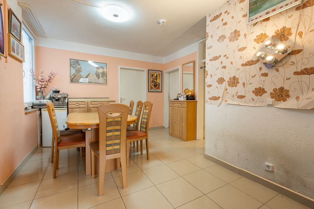 Esszimmer mit Holztisch, sechs Stühlen und dekorierter Wand, heller Fliesenboden.