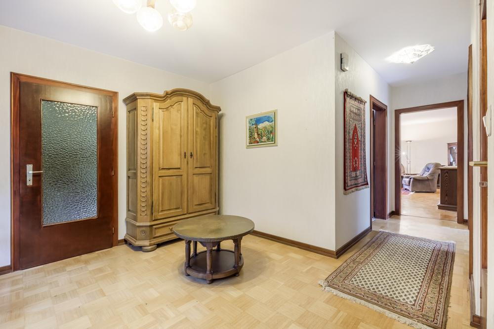Flur mit Holzschrank, rundem Tisch, Teppichen und Wandbild in einer Wohnung.