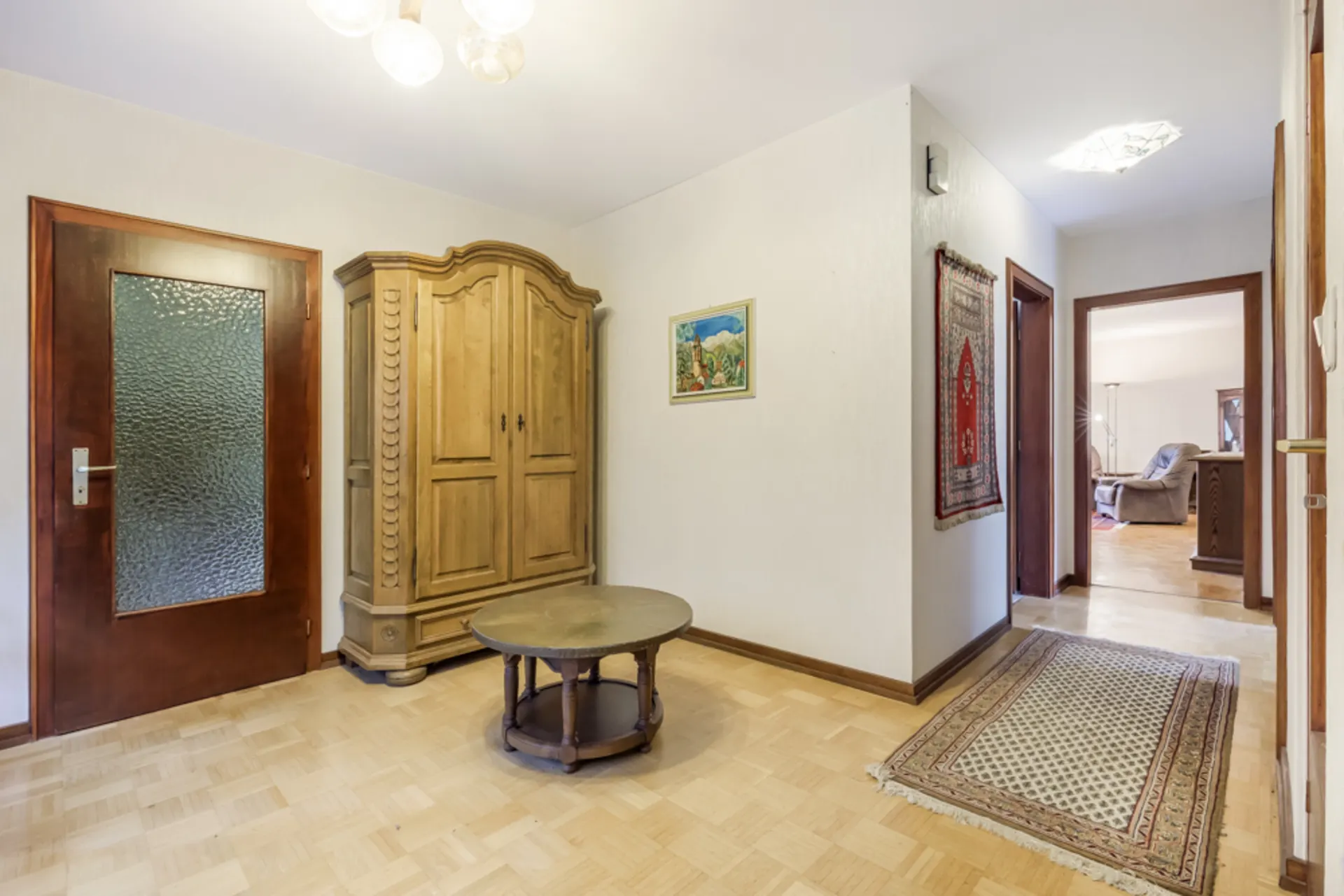 Flur mit Holzschrank, rundem Tisch, Teppichen und Wandbild in einer Wohnung.
