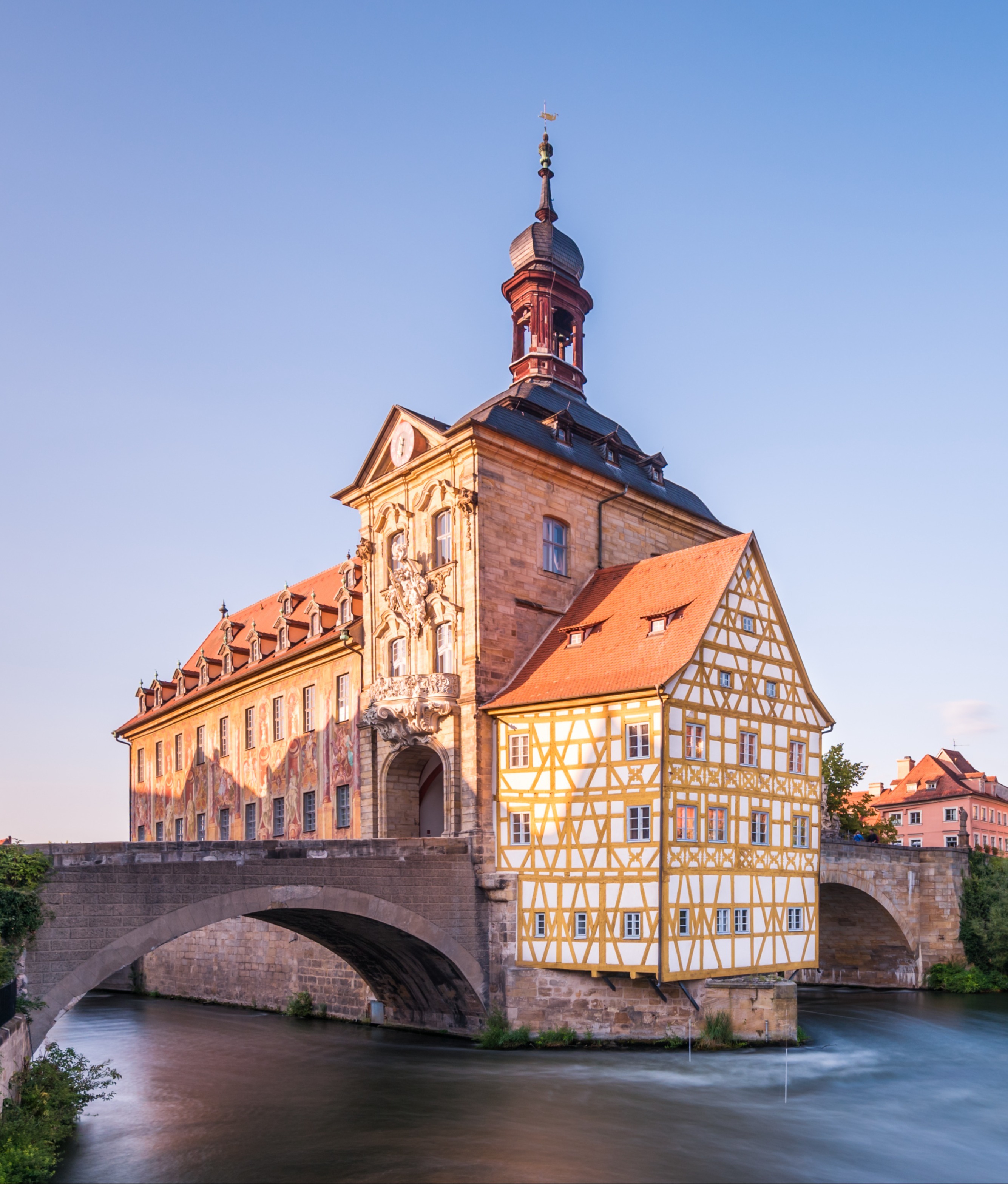 Historisches Fachwerkhaus mit Turm auf einer Brücke über einem Fluss bei Tageslicht.