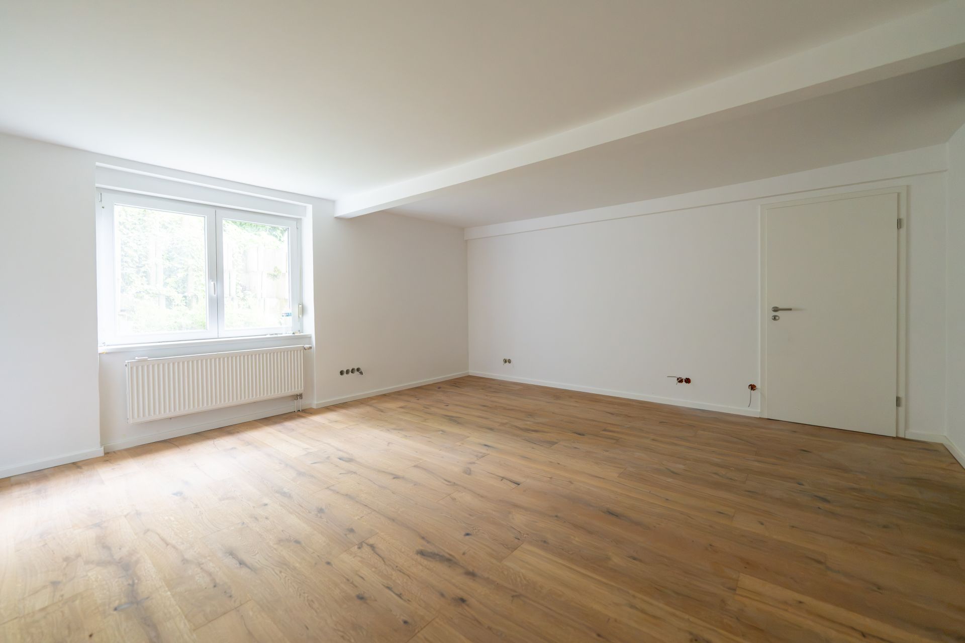 Leerer Raum mit Holzfußboden, weißer Wand, Fenster und Tür.