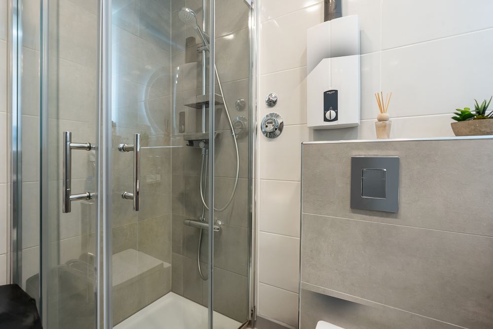 Modernes Badezimmer mit Glasdusche, Wandtoilette und kleinen Dekos auf der Abstellfläche.