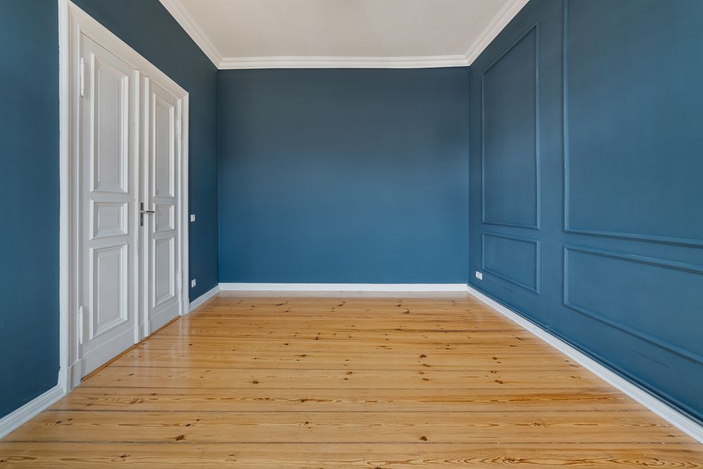 Leerer Raum mit blauen Wänden, Holzboden und weißen Doppeltüren.