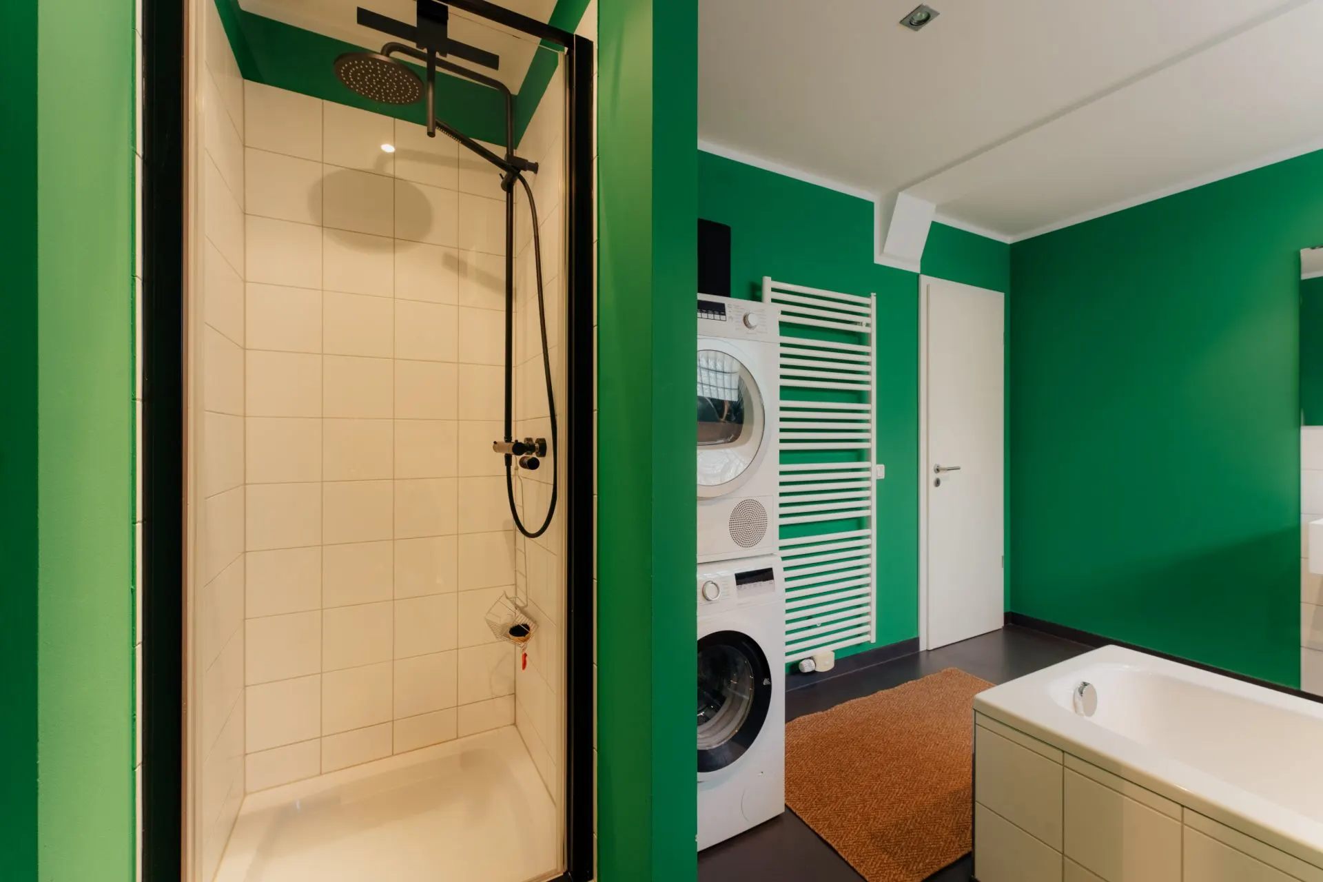 Modernes Badezimmer mit grünen Wänden, Dusche, Badewanne und Waschmaschine mit Trockner.