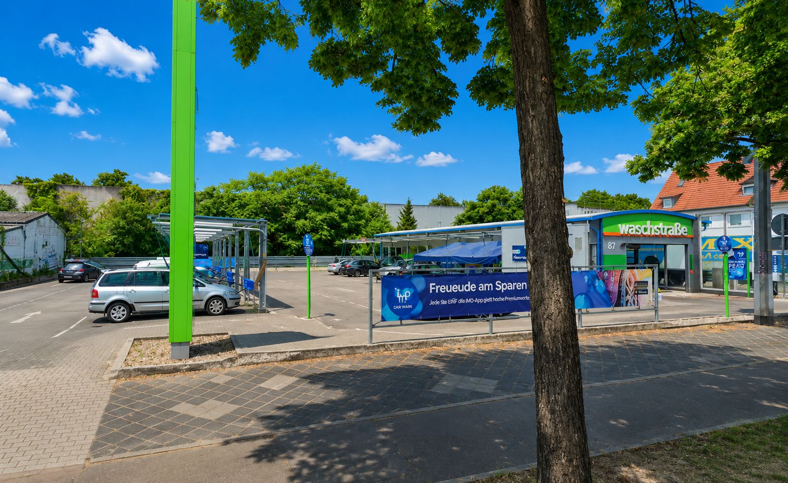 Parkplatz mit mehreren Autos, Werbebanner und einer Auto-Waschanlage im Hintergrund.