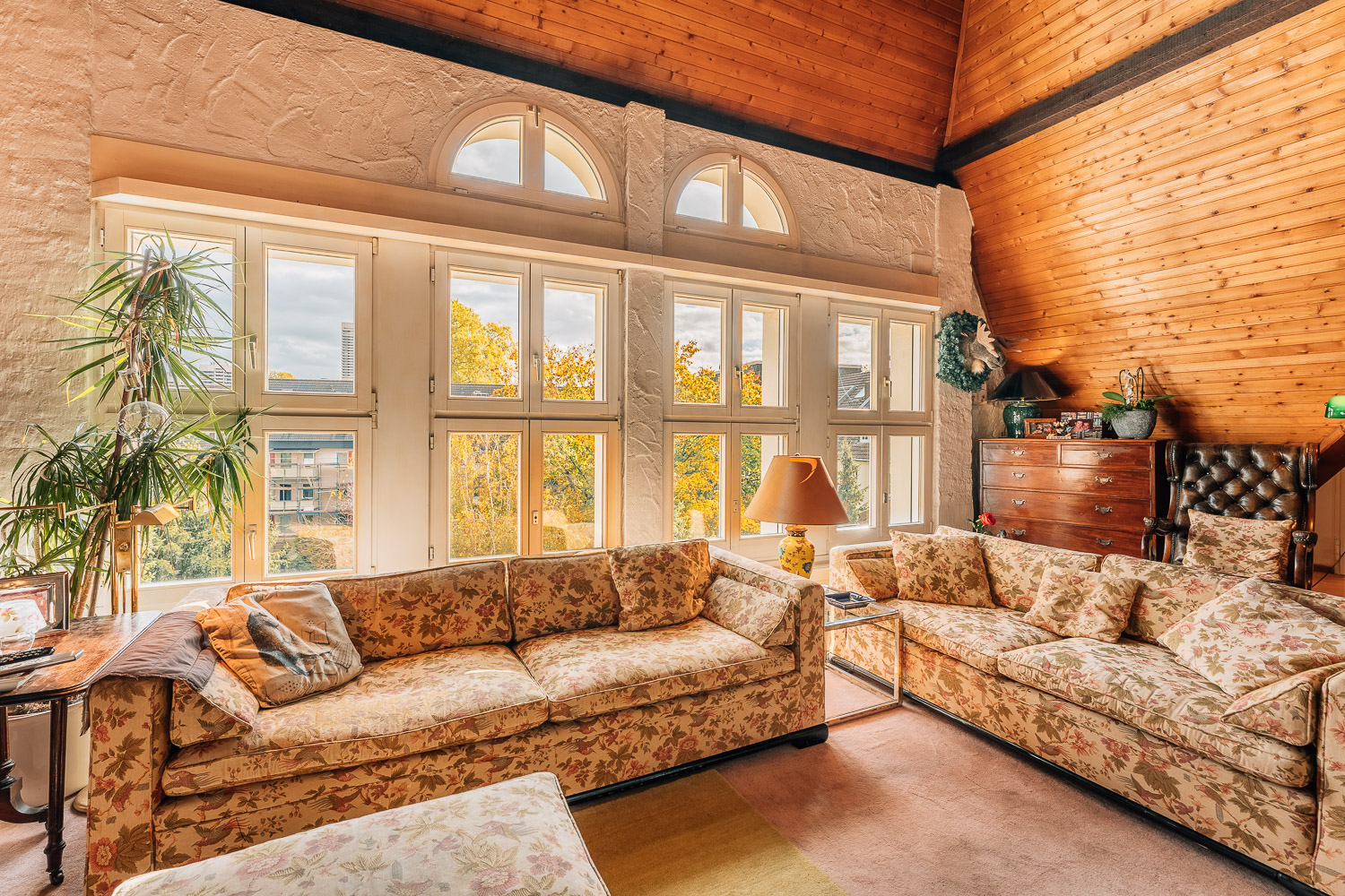 Gemütliches Wohnzimmer mit floralen Sofas, großen Fenstern und Holzwänden.