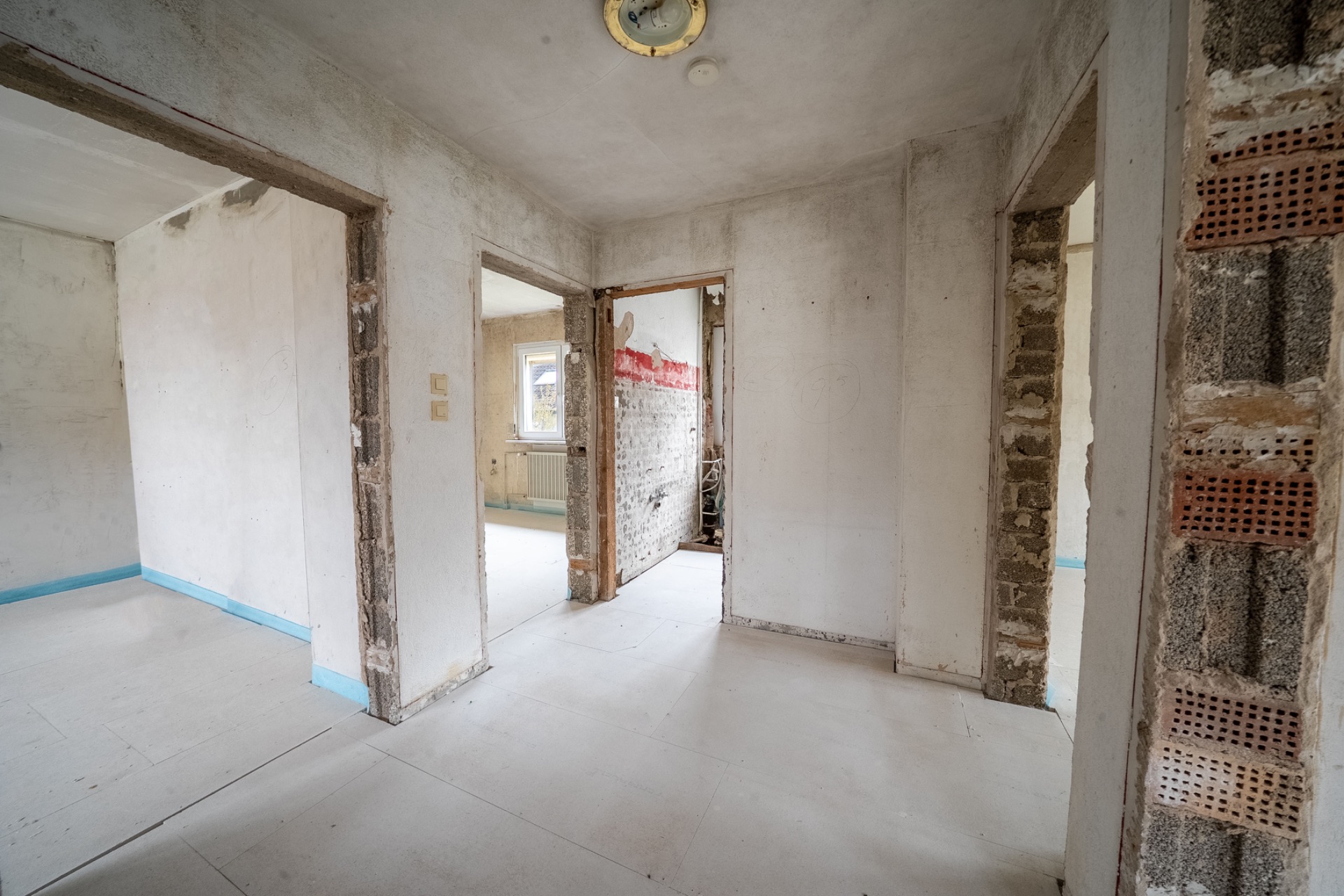 Unrenovierter Flur mit offenen Türrahmen und kahlen Wänden in einer Wohnung.