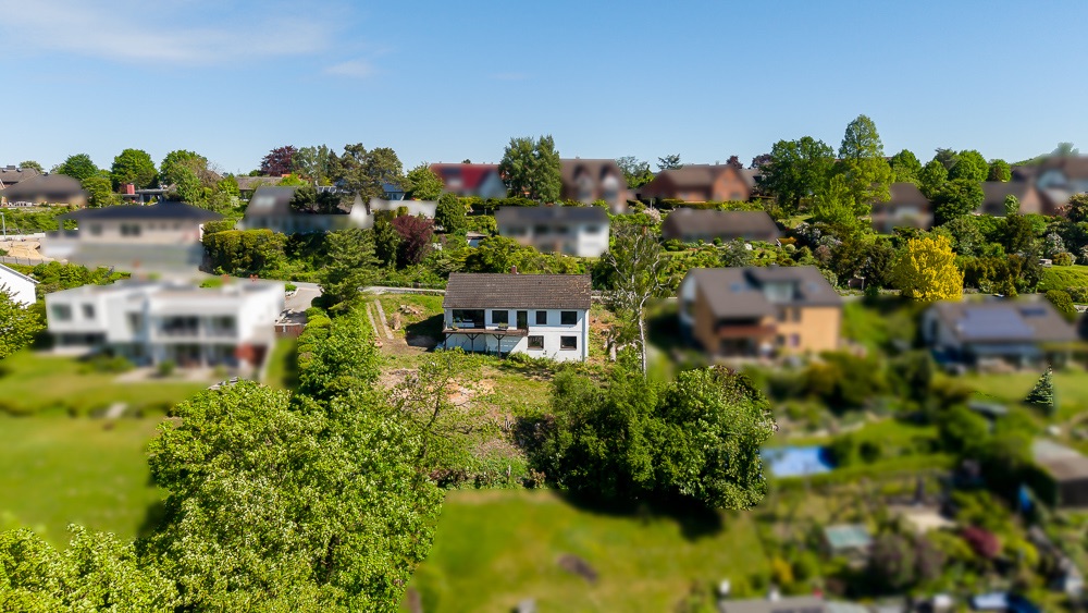 Luftaufnahme eines Einfamilienhauses mit Garten und umliegenden Wohnhäusern.