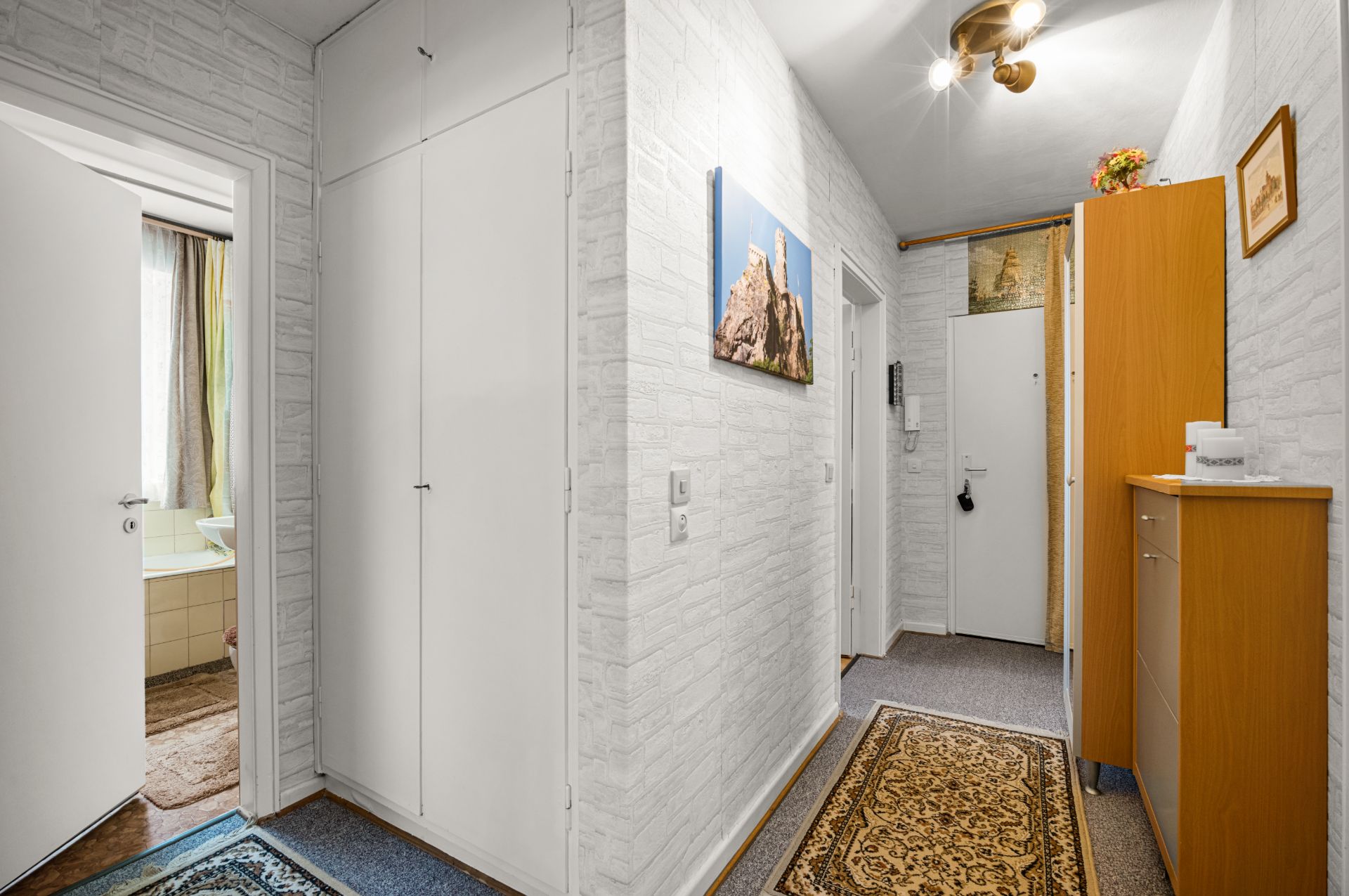 Heller Flur mit Teppich, weißen Türen, Schrank und Bildern an den Wänden.