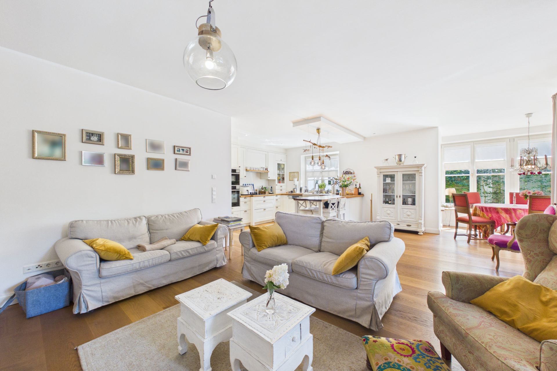 Helles Wohnzimmer mit zwei Sofas, einem Sessel und offener Küche im Hintergrund.