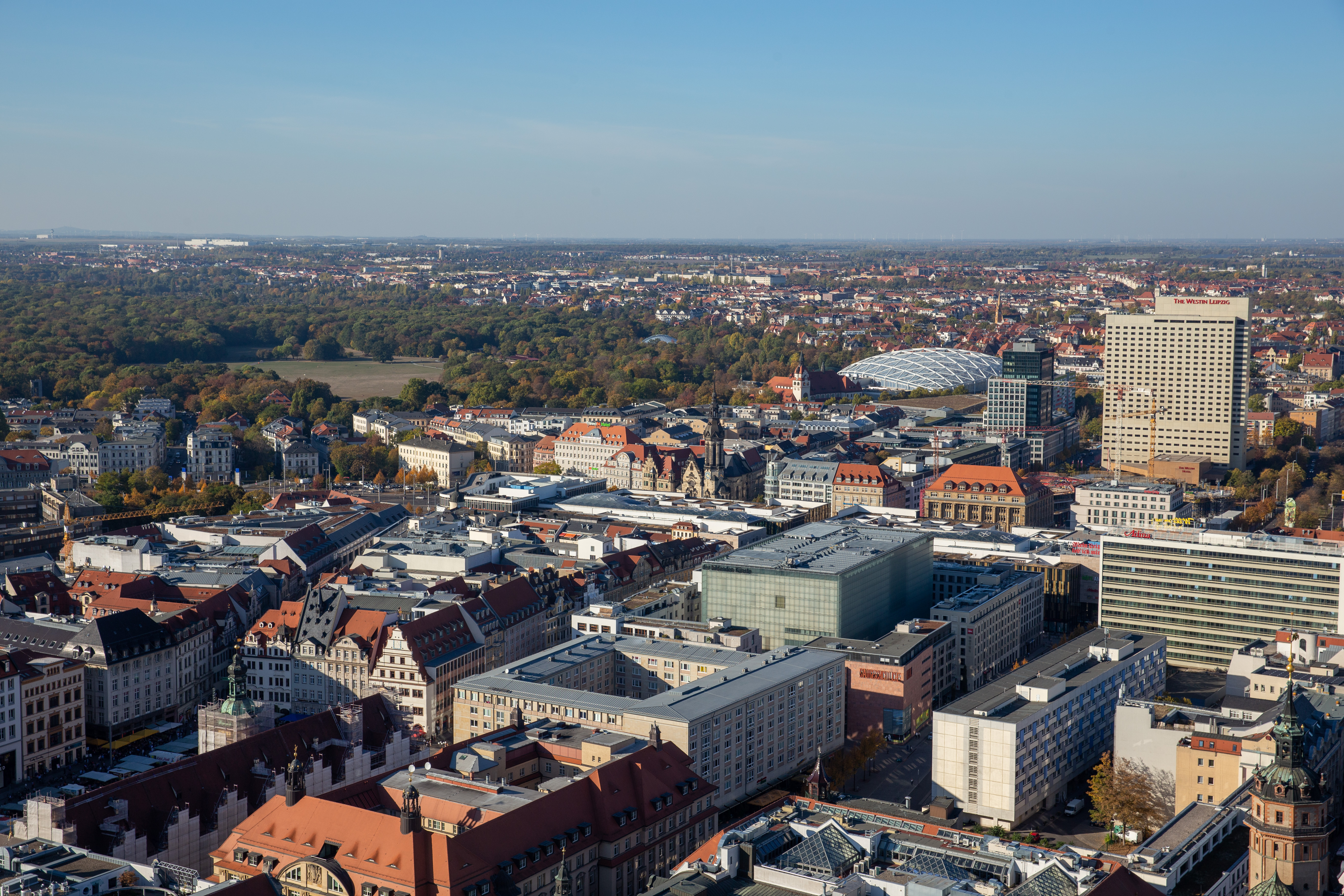 Stadtansicht mit vielen Gebäuden, roten Dächern und Parkanlagen im Hintergrund.
